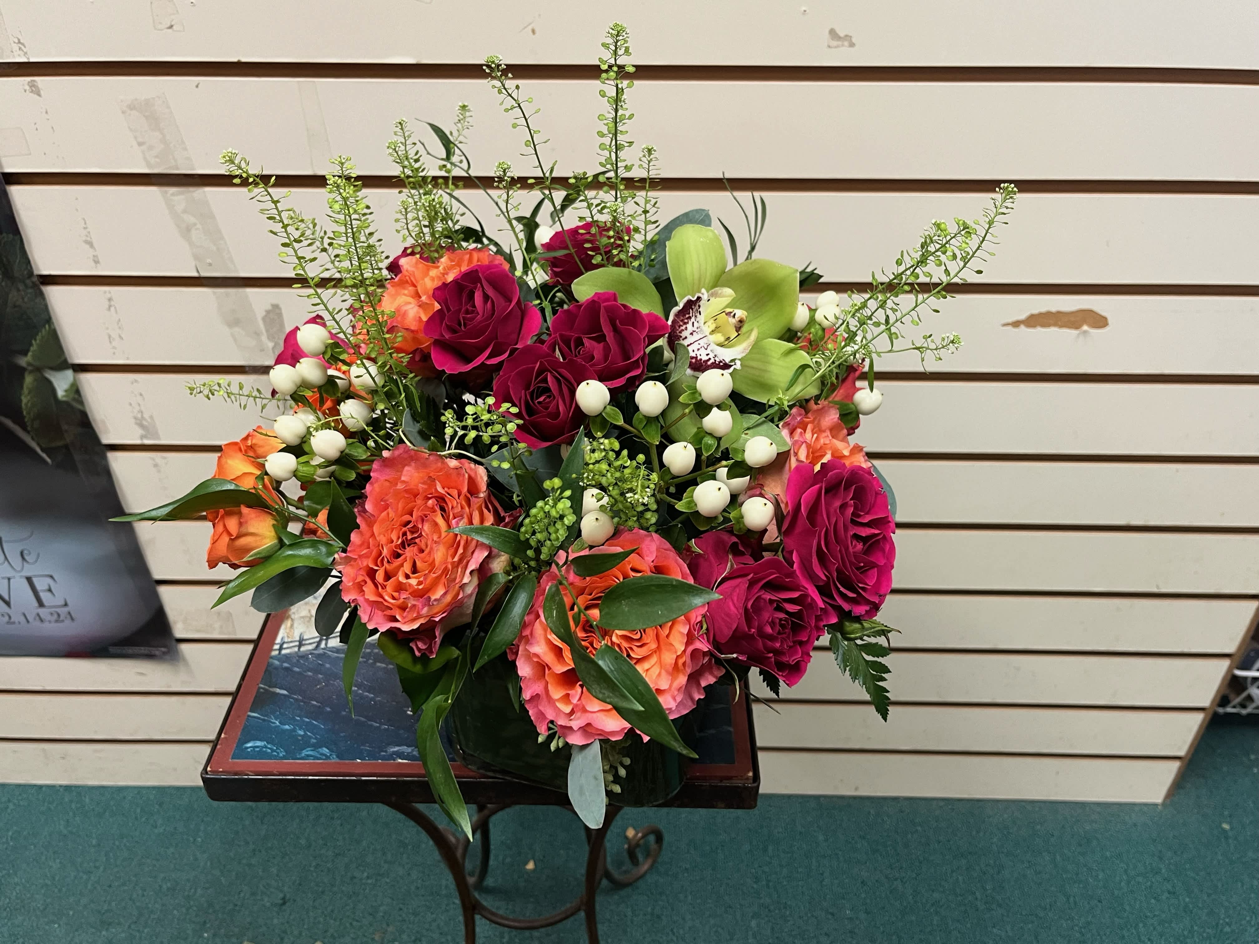 Sunset by Ashley's  - Assorted hot pinks and oranges roses and spray roses with accents of greens flowers and fillers in a cube with mixed greens  