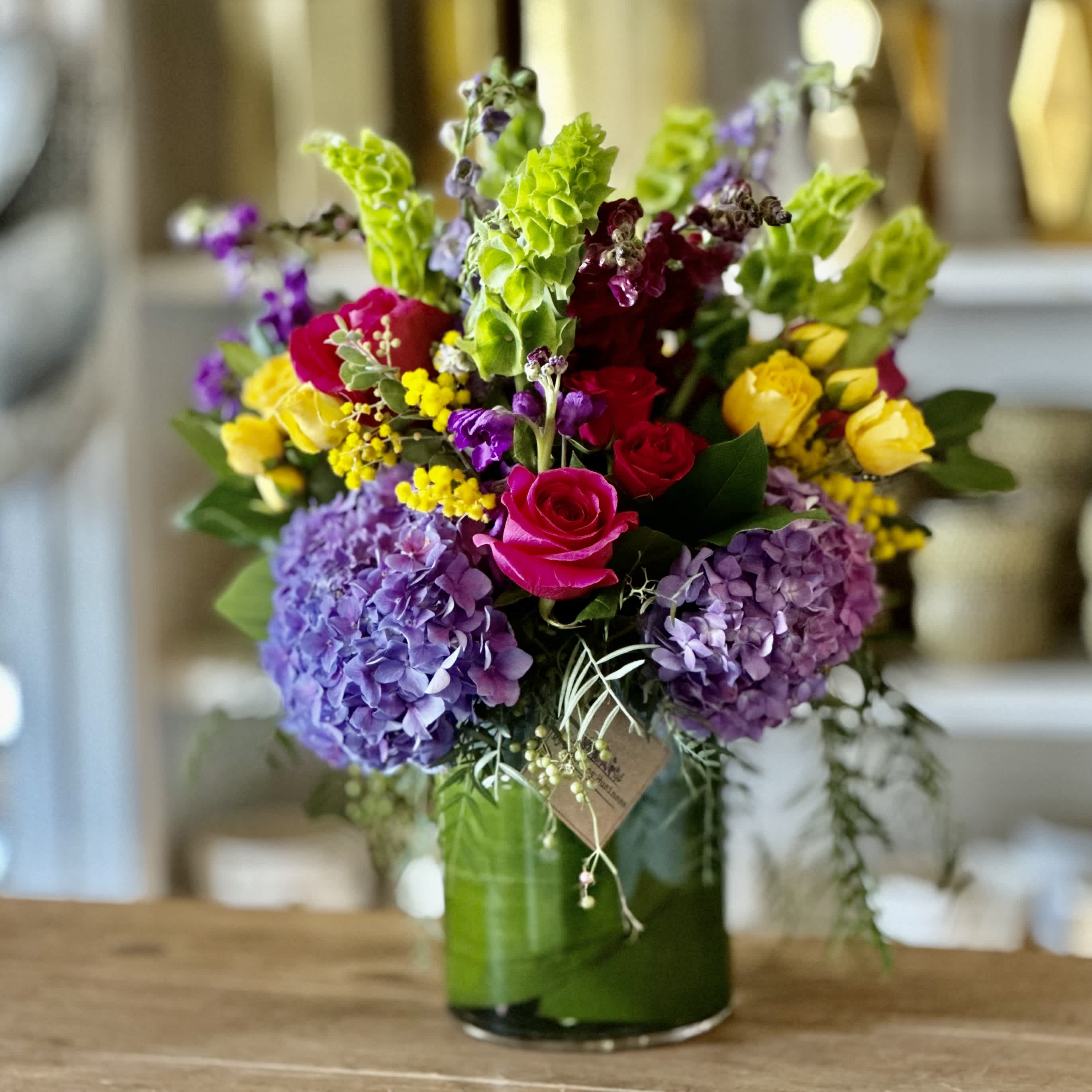 Pretty Young Thing  - Cheerful and bright is what you get with our P.Y.T. Arrangement. Clear Cylinder vase filled with bright color florals such as hydrangea's, roses, spray roses to cheer, congratulate, or show them your thinking about them. 