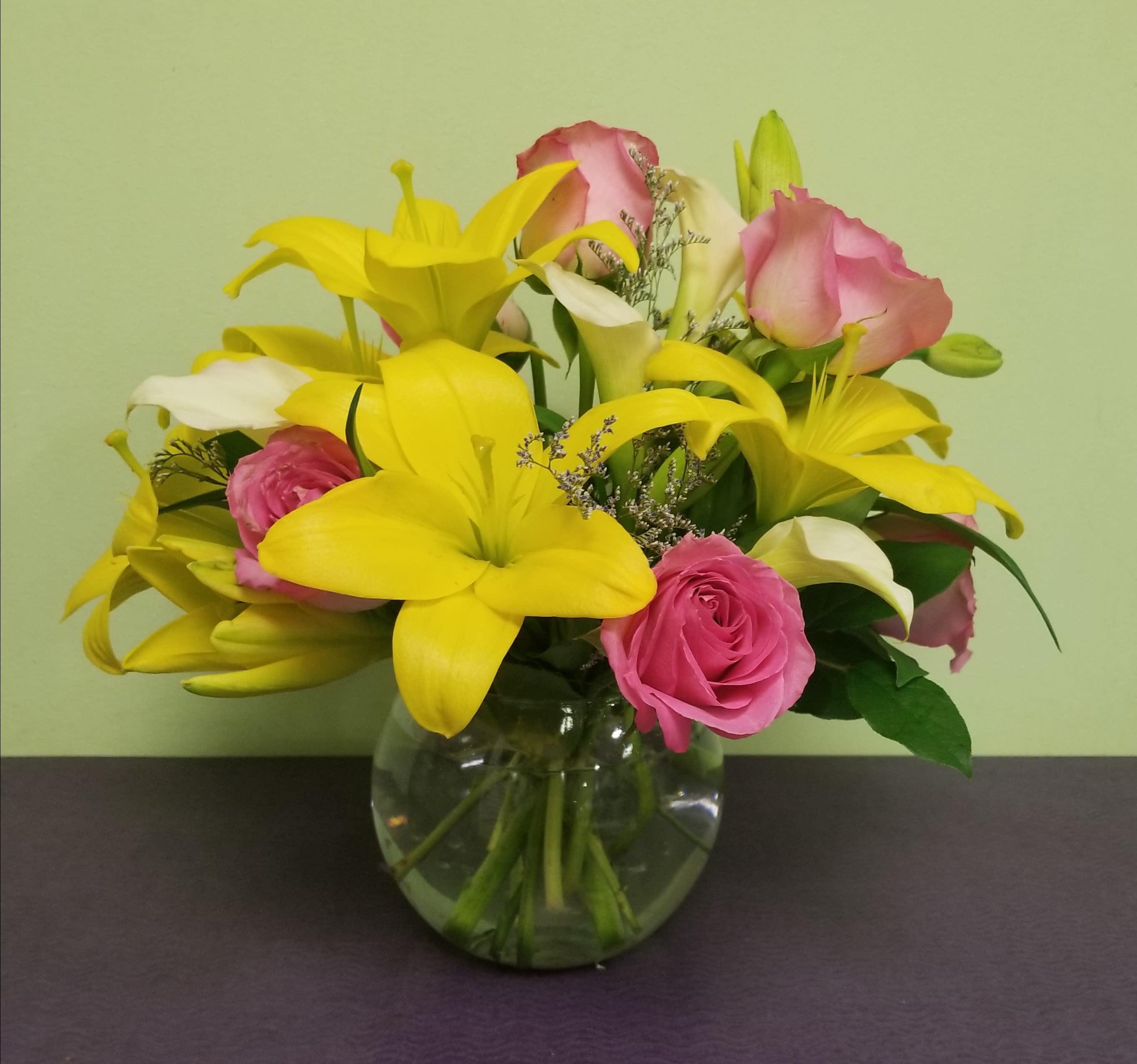Spring Meadow - This is a simple arrangement that includes bright yellow Lilies, pink Roses, rich white Calla Lilies, and purple filler. 