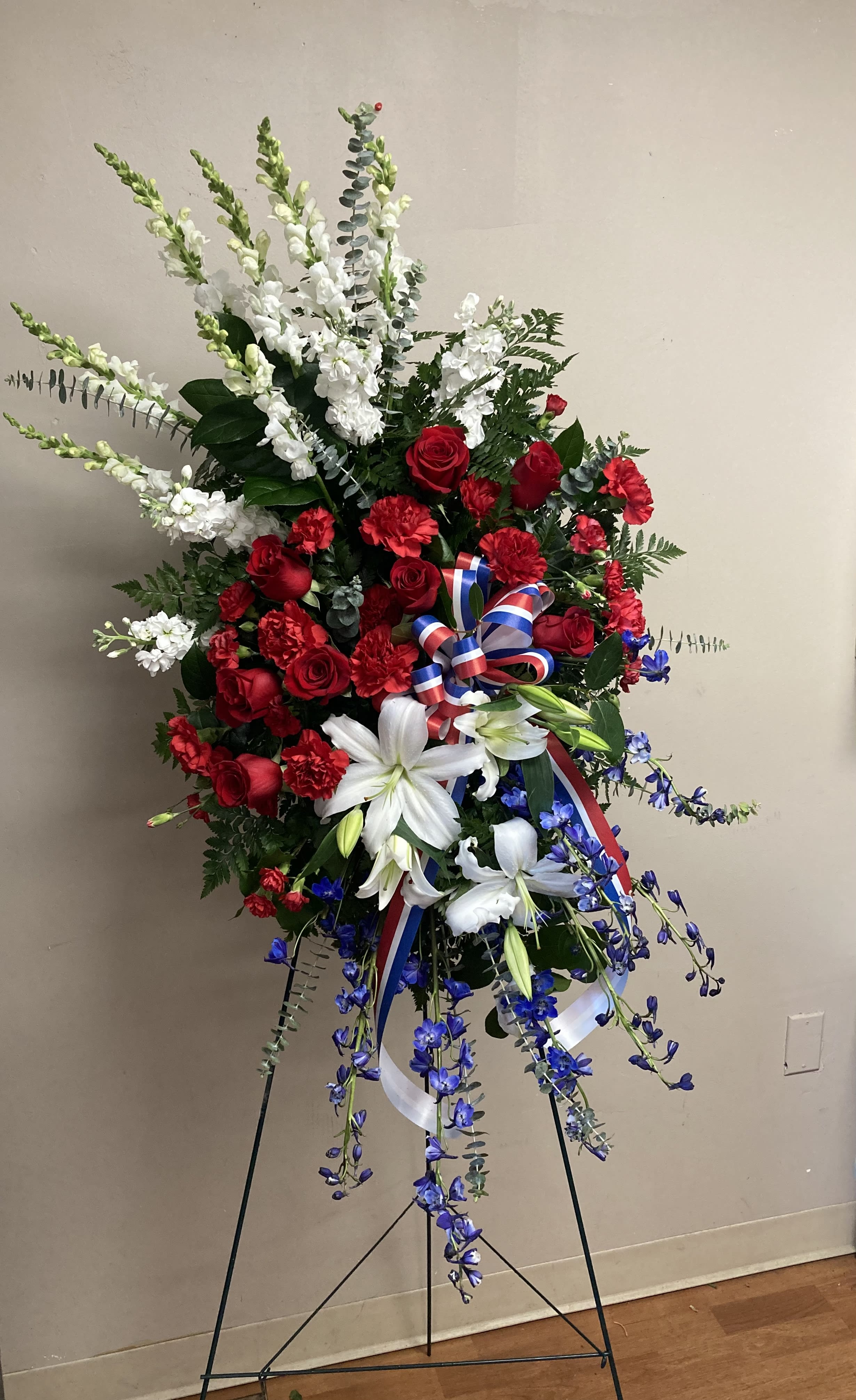 Honorable - Stunning funeral spray featuring red, white and blue. Snapdragons, delphinium, roses, lily and carnations.  Lovely honor for a loved one.