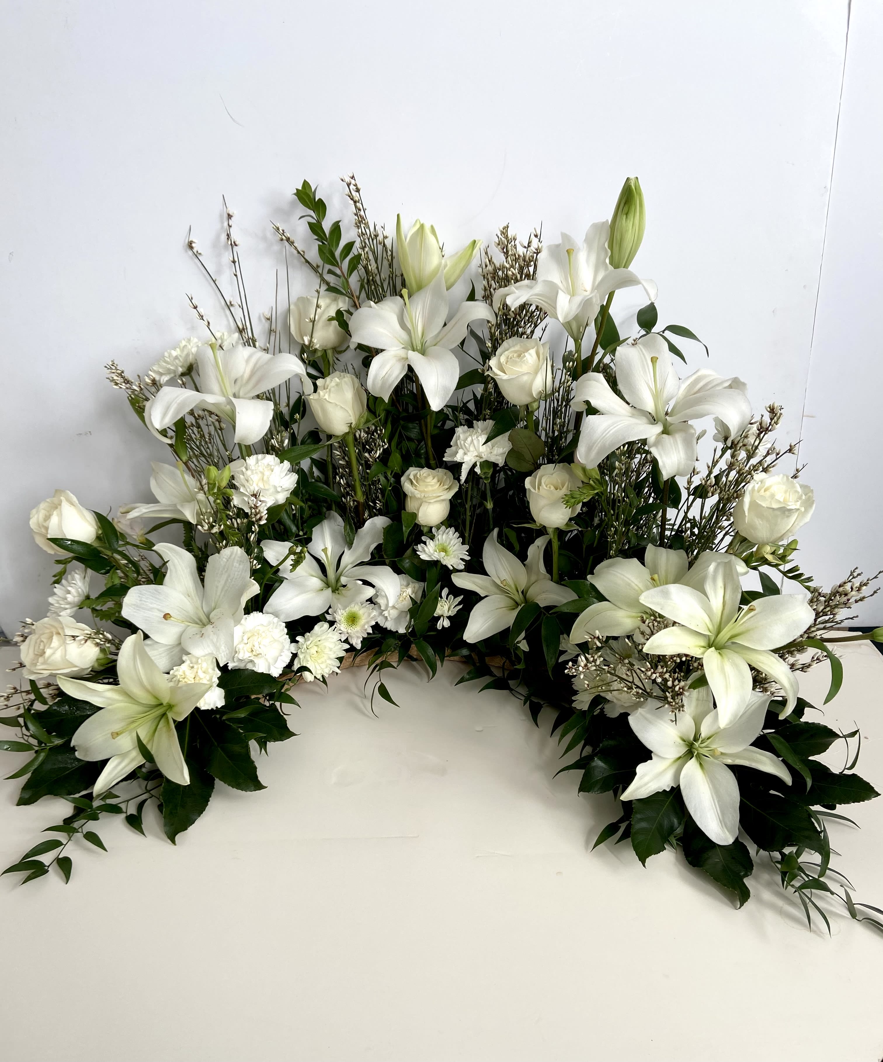 White Serenity  - Half circle memorial for urn or chest with white lilies, white roses, carnations, mums and genestre 
