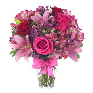 European Romance Bouquet - This flirtatious combination of Asiatic lilies, waxflower, alstroemeria and roses makes a thoughtful gift they'll not soon forget. A pretty pink ribbon and clear fluted glass vase add to the romantic look. 