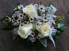 White Rose Wrist Corsage - Accent your formal wear with stunning flowers! Always in Season has an extensive collection of corsages, wristlets, and boutonnieres perfect for homecoming, prom, weddings, or any formal occasion.  Accent your gown, tux, or any formal dress with our gorgeous floral designs!  We customize each wrist corsage with matching accents of ribbon, diamonds, beads or accents. Please note in your order if you would like any other color of ribbon.  Standard design includes bracelet, spray roses, accent filler flowers, and bow  Deluxe design includes bracelet, spray roses, accent filler flowers, bow and either pearls or rhinestones.  Premium design includes bracelet, spray roses, accent filler flowers, bow, rhinestones or pearls and bling design with upgraded bracelet.   