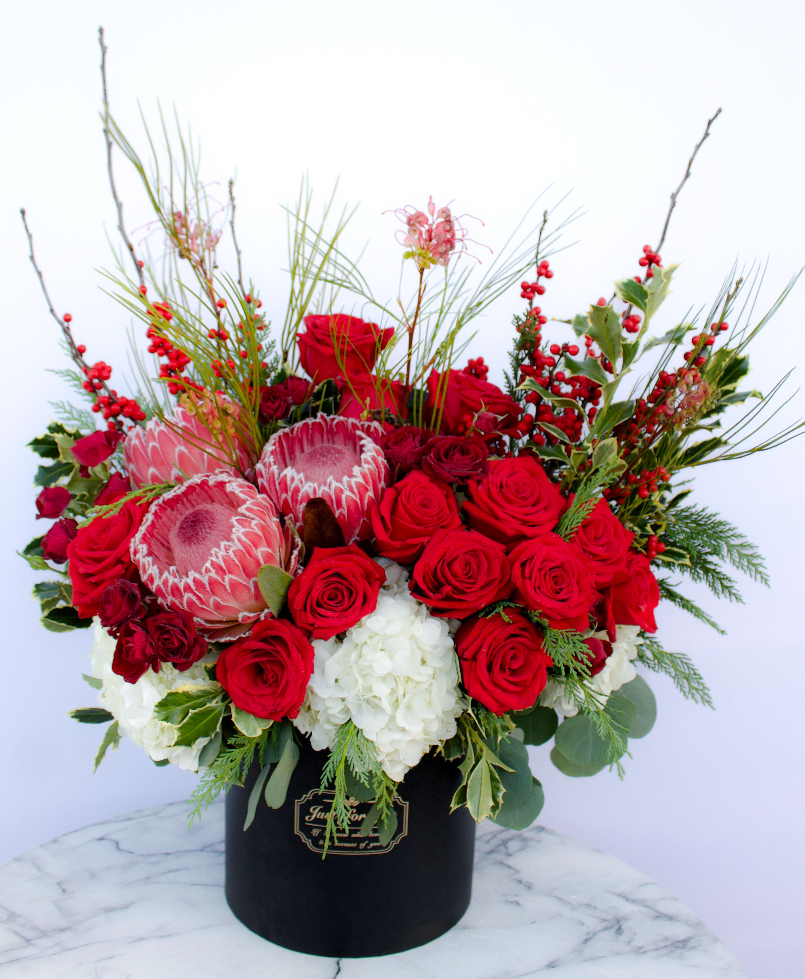 Mesmerizing Beauty - Breathtaking blooms crafted with grandeur and mesmerizing beauty designed to captivate the senses! With the velvety red roses and premium proteas on a bed of lush white hydrangeas arranged in a keepsake black box, this bouquet is a definite stunner your loved one truly deserves.  An elite ensemble and bestseller all year long!  Due to high volume demand, please order in advance to guarantee availability and timely delivery before Valentine’s Day!  Approximately 23” H x 16” W