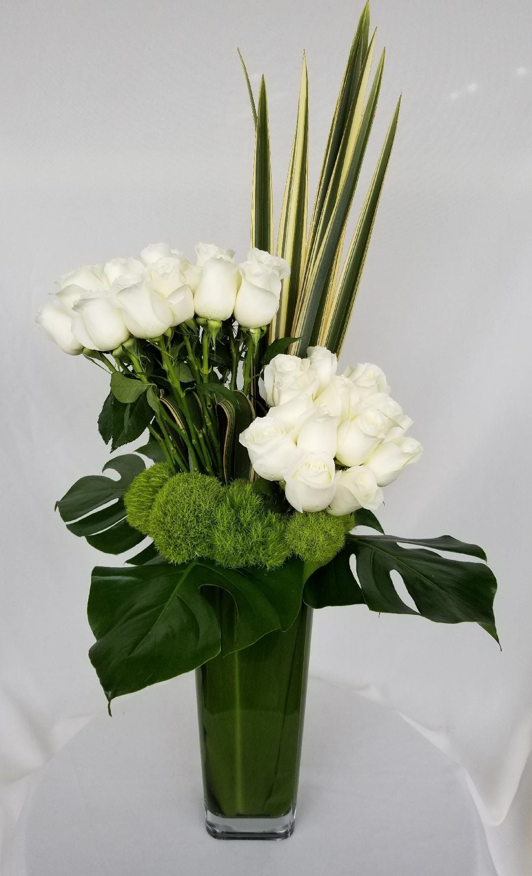 Wilshire Whites  - L.A.'s Eternal Elegance: Pure White Roses Dance with Emerald Dianthus (Santa Monica, Hollywood, Pasadena, Beverly Hills, West Hollywood) This Valentine's Day, transcend the ordinary in Los Angeles with a love story whispered in purest white. Imagine ethereal long-stemmed roses, their ivory petals bathed in moonlight, entwined with a lush embrace of Green Trick Dianthus, their emerald whispers adding a touch of playful charm. This captivating arrangement, cradled in a towering glass vase, isn't just flowers; it's a timeless tale of devotion, crafted in nature's most delicate hues, ready to capture your sweetheart's heart with its everlasting elegance.  More Than Just Breathtaking Blooms:  L.A.'s Love Sonnet in White: Our skilled florists are love's whisperers, meticulously weaving each rose and dianthus into a symphony of enduring affection. Prepare for whispered &quot;I do's&quot; and stolen glances when you unveil this ethereal declaration. Locally-Sourced Purity: We hand-pick only the freshest, most radiant white roses and vibrant dianthus from trusted L.A. growers, ensuring long-lasting brilliance and intoxicating fragrances that linger like whispered promises in the evening breeze. Beyond February 14th: Rekindle the timeless flame anytime! This versatile masterpiece shines on anniversaries, weddings, or simply as a reminder that your love blooms with eternal elegance. Blooming Convenience for Busy Romantics:  Skip the L.A. traffic and let love blossom at your doorstep. We offer convenient flower delivery across Santa Monica, Hollywood, Pasadena, Beverly Hills, and West Hollywood with same-day or scheduled options. Speak Beyond Words: Let this captivating bouquet do the talking for your heart. Add a personalized message to make your gift even more special and ignite a spark of joy in your loved one's eyes. Sustainable Love Stories: We're committed to eco-friendly practices, sourcing our flowers responsibly to ensure your love story blossoms beautifully for the planet too. Ready to whisper your love story with flowers this Valentine's Day? Contact Dave's Flowers today and let our blooming artists craft a pure white masterpiece that reflects the unwavering devotion and timeless elegance of your love story. Explore our world of blooming sonnets and make every moment a whisper of forever in the heart of L.A.