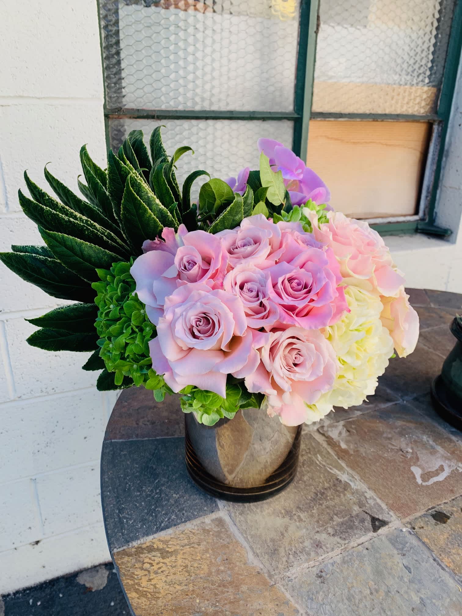 Arcadia Pastel - Nice chrome glass vase with garden roses, Hydrangeas and orchids with lush beautiful large greens.