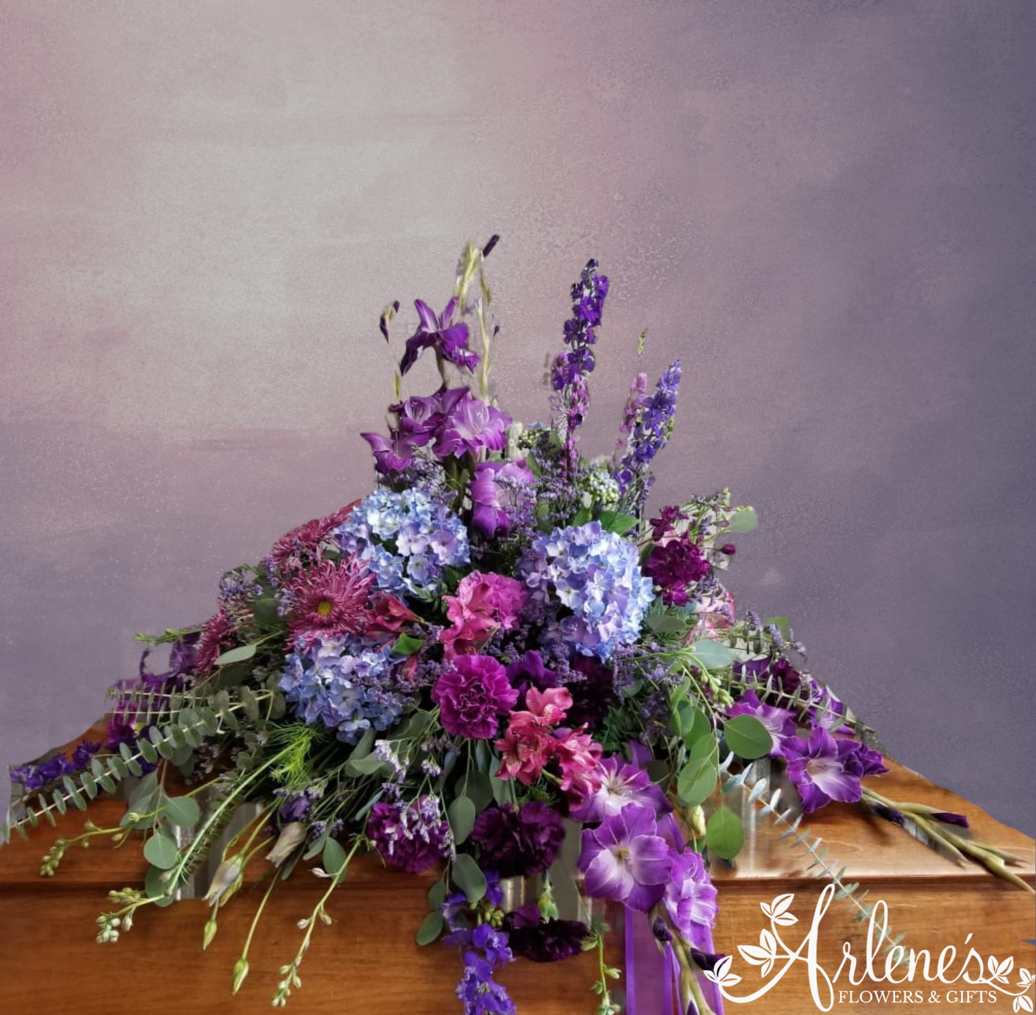 Purple Mountain Majesty Casket Spray Purple Mountain Majesty Casket Spray - A majestic send off, a taller spray bursting with blue and purple hues. Gladiolas, hydrangea (may use silk), larkspur, delphinium and more.