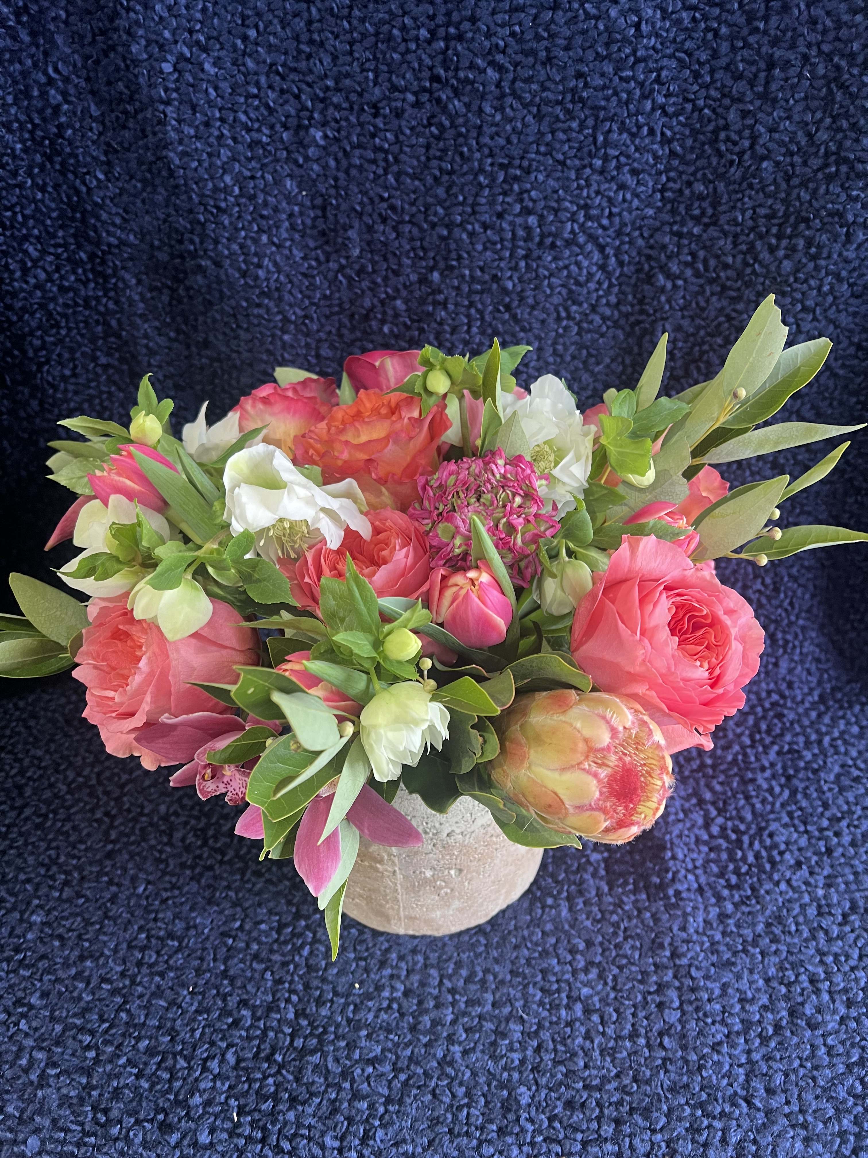 Coral Flame Coral Flame - Grandiflora protea accented with free spirit, candy expression tulips, ranuculus, mini-cymbidium orchid and hellebore. Finished with bay leaves in a rustic cylinder lightly dusted with copper.