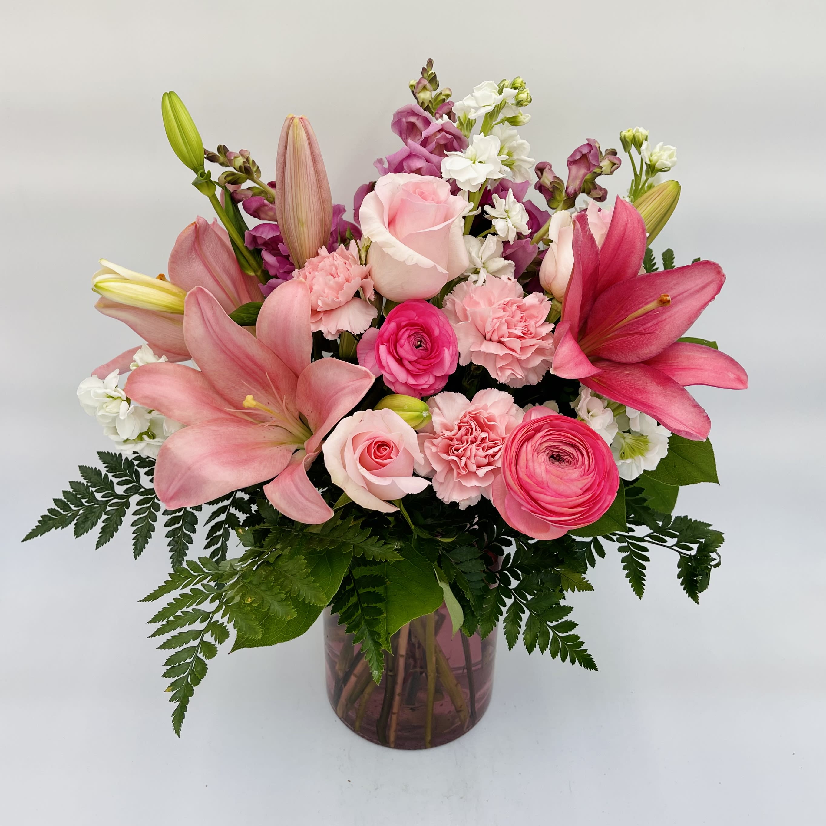 Everything Pink blooms Bouquet - Pink blooms overflowing in a pink glass vase will make her extra sweet.  Arrangement includes pink roses, ranunculus, lilies, carnations, snapdragons, accented with white stock and greenery.