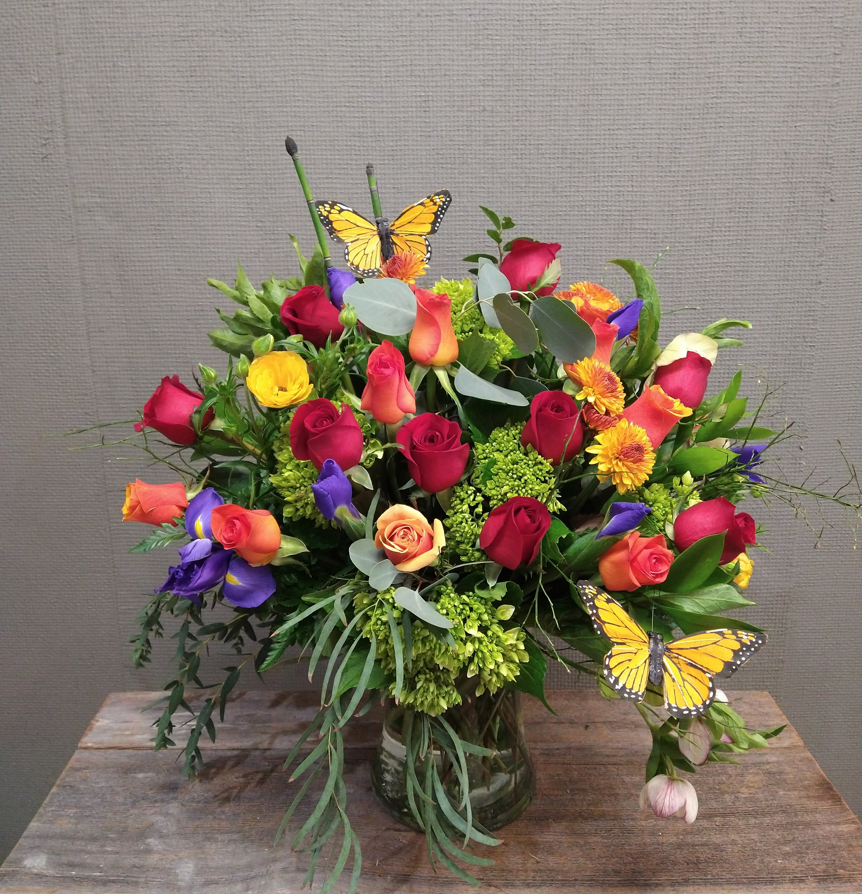Now and Always - For the enduring love. A statement arrangement with two dozen roses in red and orange, surrounded by blue iris and other seasonally available high-end flowers in jewel tones, such as hydrangea, viburnum, ranunculus, hellebores, dahlia, anenome, etc. We will do our best to accommodate any requests for colors or flowers; please let us know in special instructions.