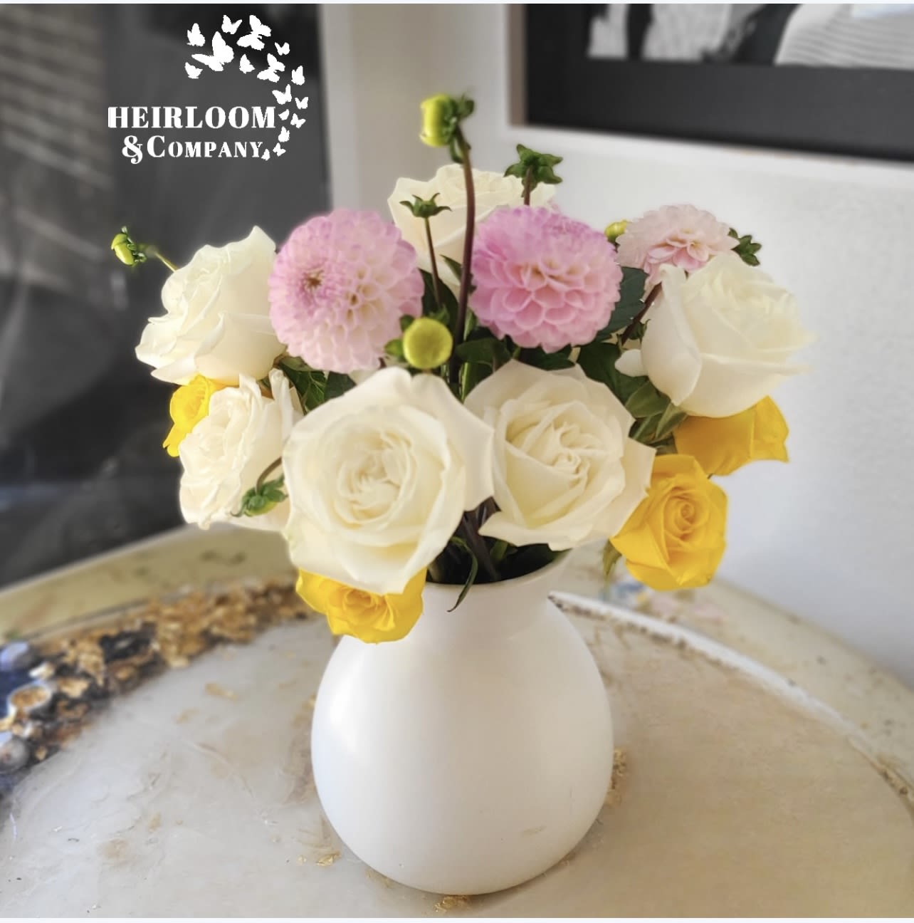 Fairy Face  - This charming arrangement features a captivating blend of blush pink dahlias, sunny yellow roses, and pristine white roses, all carefully hand-picked to create a harmonious symphony of colors.  Nestled in a pristine white vase, this arrangement radiates the same cheerful energy that Tinker Bell brings to Neverland. Each bloom is carefully chosen to reflect the palette of happiness and brightness, making it a perfect gift to uplift spirits, celebrate a special occasion, or simply add a touch of magic to any space.. 