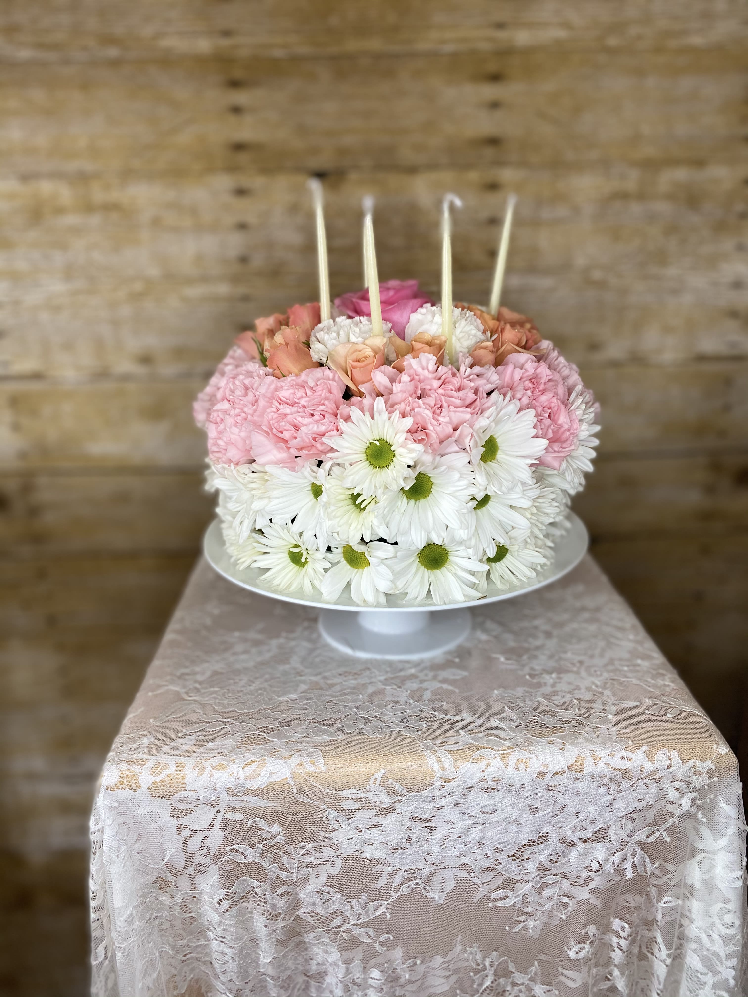 Warm Wishes Floral Cake (colors will vary) - This Floral Cake is set to celebrate their birthday with sweet surprise. Perfectly arranged in the shape and styling birthday cake presented on a white cake plate, this memorable flower arrangement will add to the festivities of their special day.