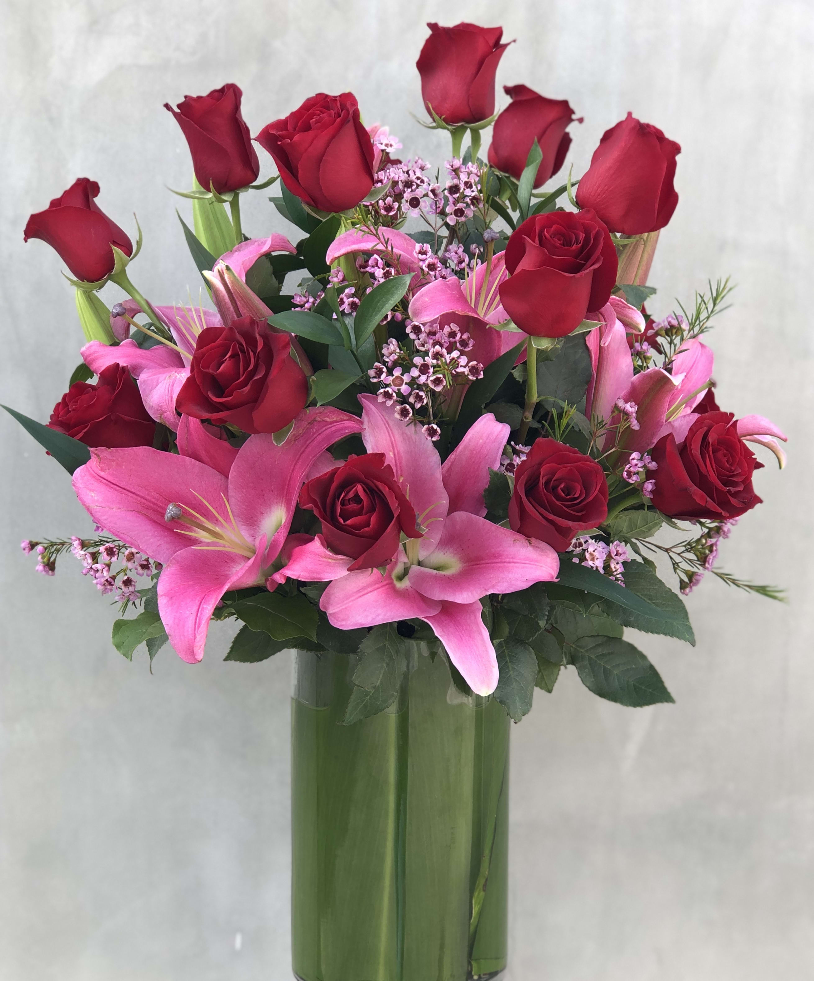 Romantic  - Classic red roses with pink lilies arranged in a tall cylinder vase filled with Ti leaves. 