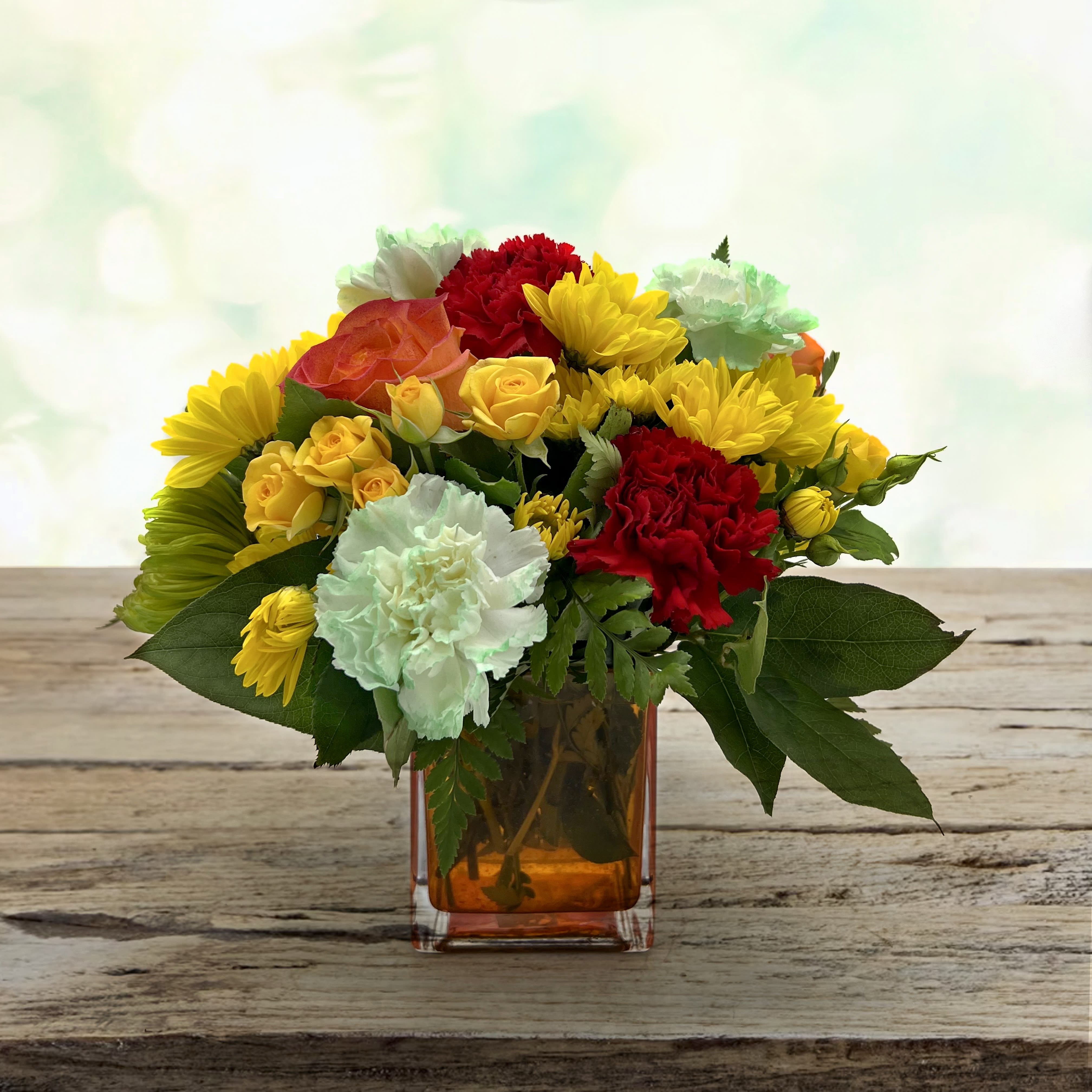 Teleflora's Citrus Smiles Bouquet - They brighten your days with their friendship and love brighten theirs with these bold and beautiful blooms! Hand-delivered in a stylish glass cube a gift in and of itself - this spirited mix of roses carnations and mums is sure to make them smile!