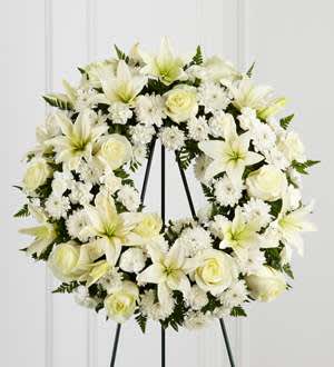 The FTD® Treasured Tribute™ Wreath - The FTD® Treasured Tribute™ Wreath offers peaceful wishes of heartfelt sympathy with each delicate bloom. Bright white roses, Asiatic lilies, mini carnations and cushion poms are beautifully arranged to form an elegant accented with lush and vibrant greens. Displayed on a wire easel, this gorgeous tribute is a wonderful symbol of eternal life and sweet serenity. Approximately 22 inches in diameter.