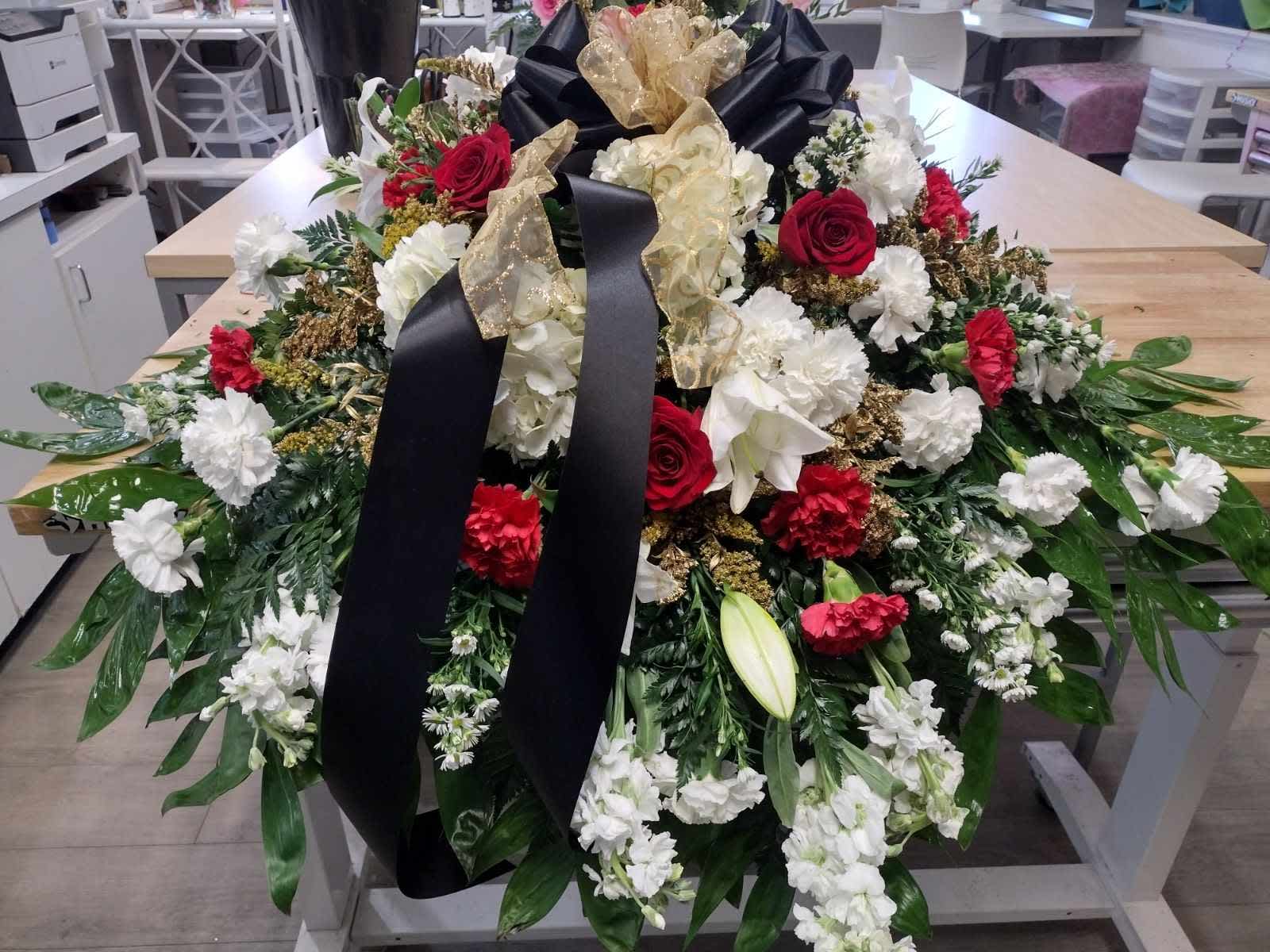Red, Black, White Casket Spray - Red/white carnations, white lillies, white stock, gold leaves, lush greenery all tied together with a beautiful black and gold bow.