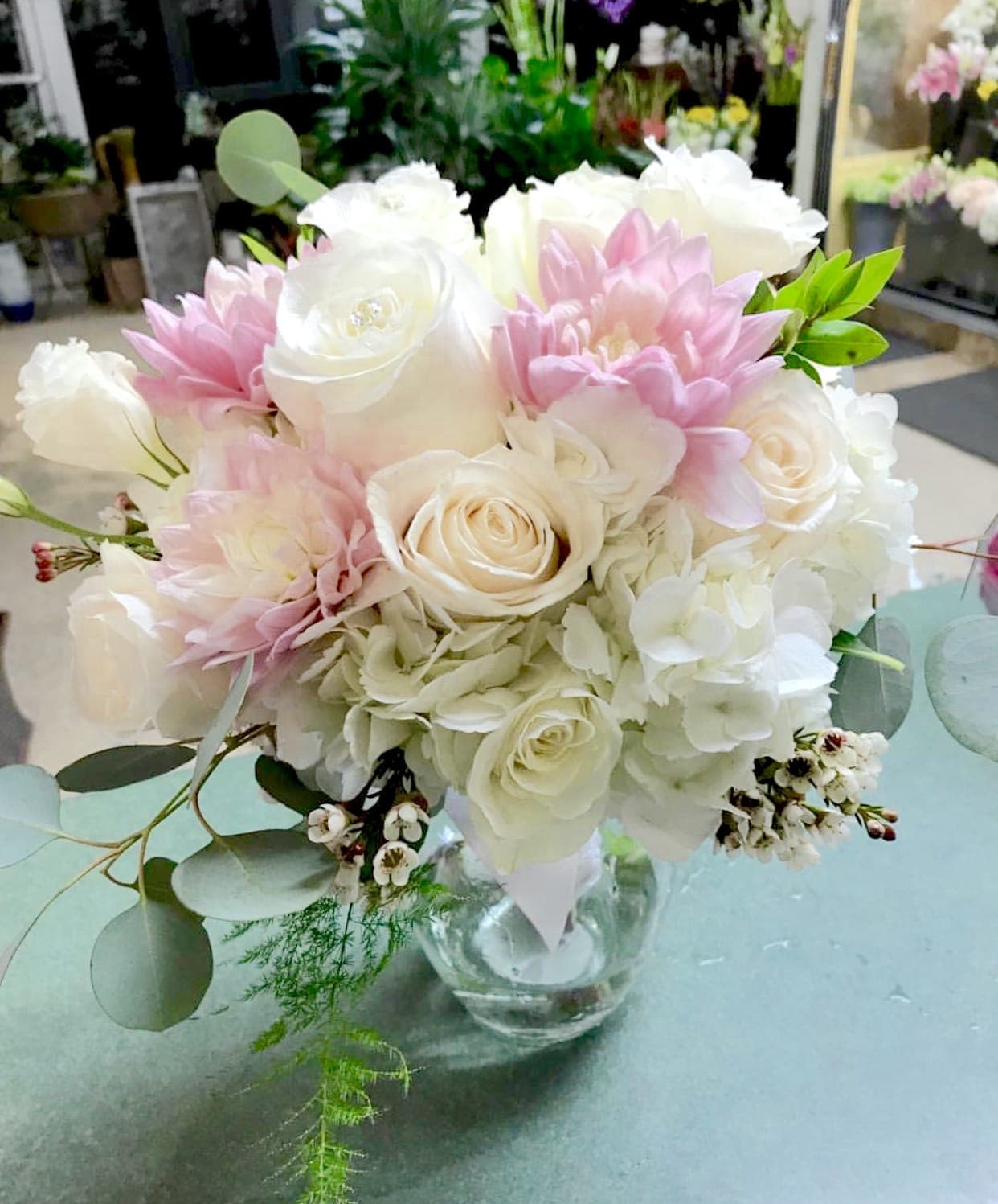 Serenity Serenity - Beautiful premium white roses and pastel dahlias in a bed of hydrangea in a clear glass vase.