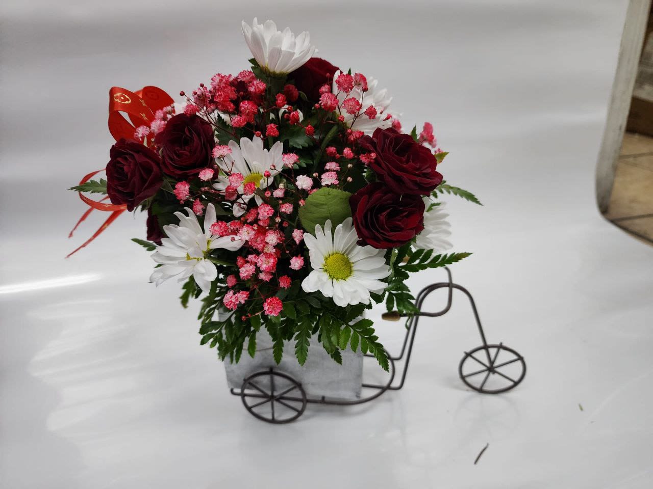 Love On Wheels - A Small Bicycle With 3 stems  red  spray roses,3 stems of white daisies ,red baby breath  and a red bun  