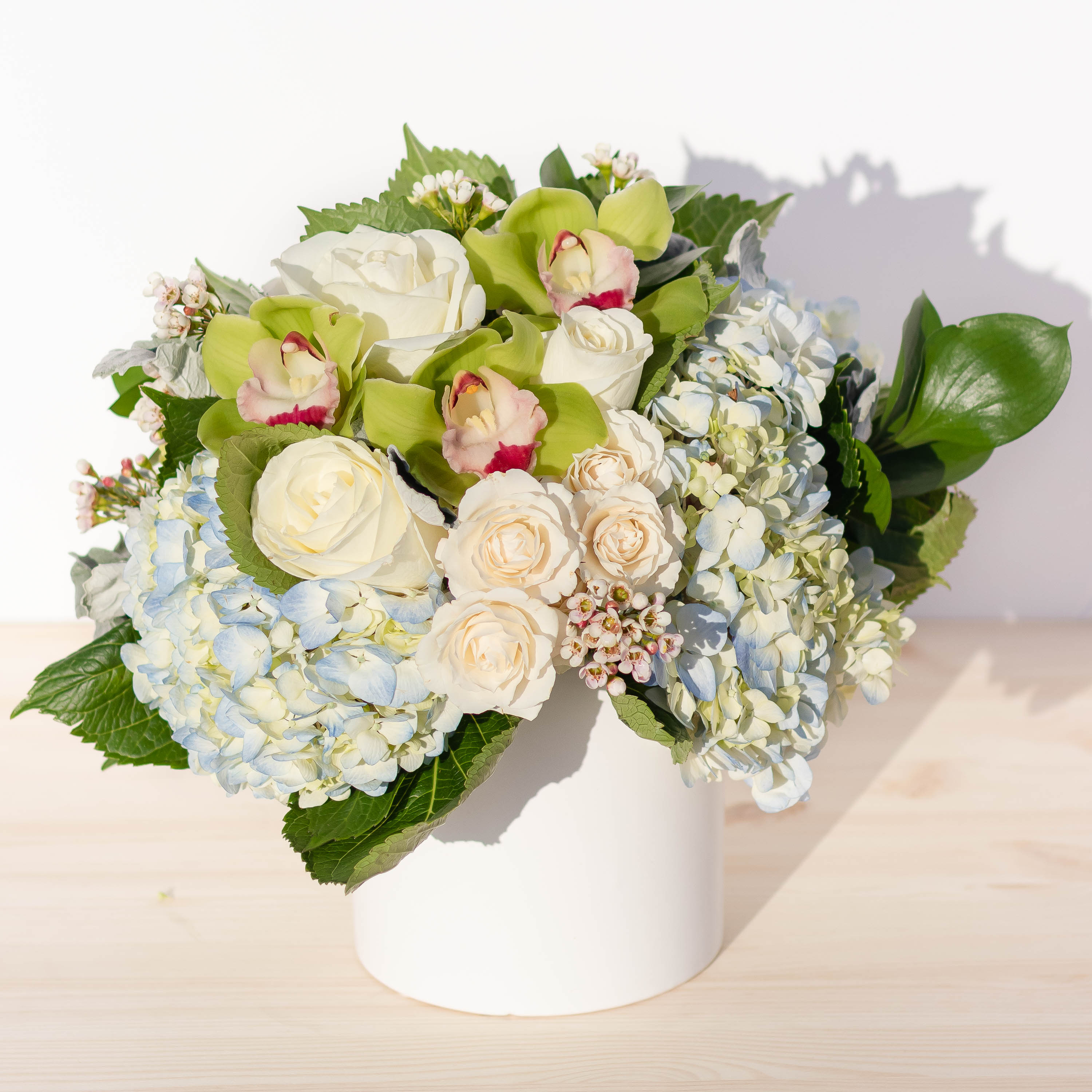 CLEAR SKIES  - Beautiful display of ivory and blue hydrangeas. Cymbidium orchids compliment this design. Set in a modern white ceramic vase.   Orientation: All-around Size: Medium  Please note: We use flowers that are available at that given time. The look and the freshness of the flowers are always the most important, therefore the arrangement may vary. We may notify you be email for any substitutions may be made based on best product available.