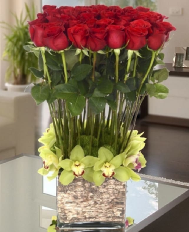 Mi Amore’ Mi Amore’ - For the Love of your Life this elegant display of long stem roses, and exquisite cymbidium orchids, accented by green dianthus is presented in a unique glass or ceramic container. Available in: Red or Pink Roses, container may vary slightly. Approximate Dimensions: 10” to 14” wide by 24” to 30” tall