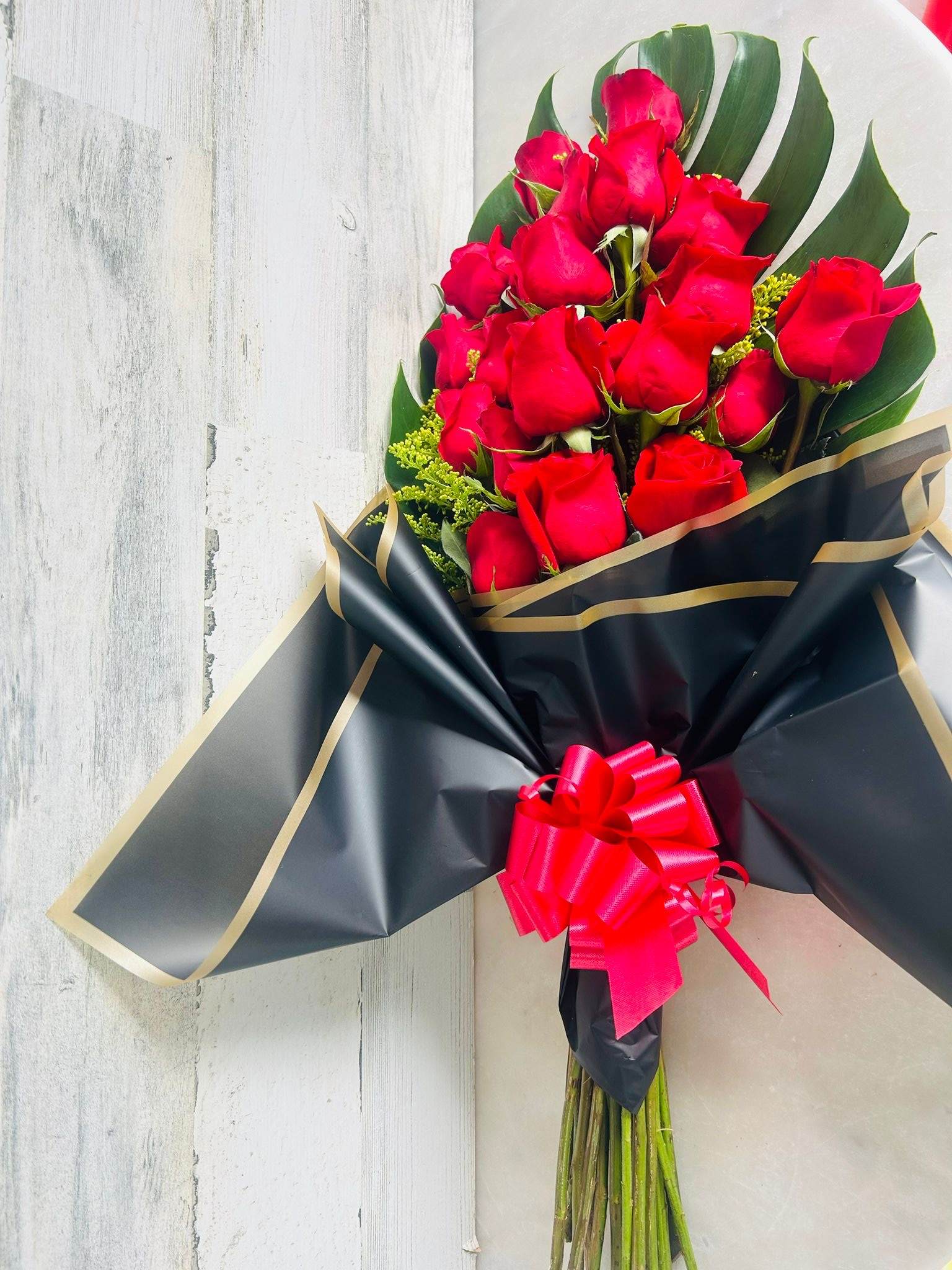 TROPICAL LOVE - 18 Red Roses covered with monstera leaf and a touch of solidago, all wrapped with a luxury black with golden lines paper and a box, excellent for any occasion. 21 roses in the deluxw version and 24 with premium   