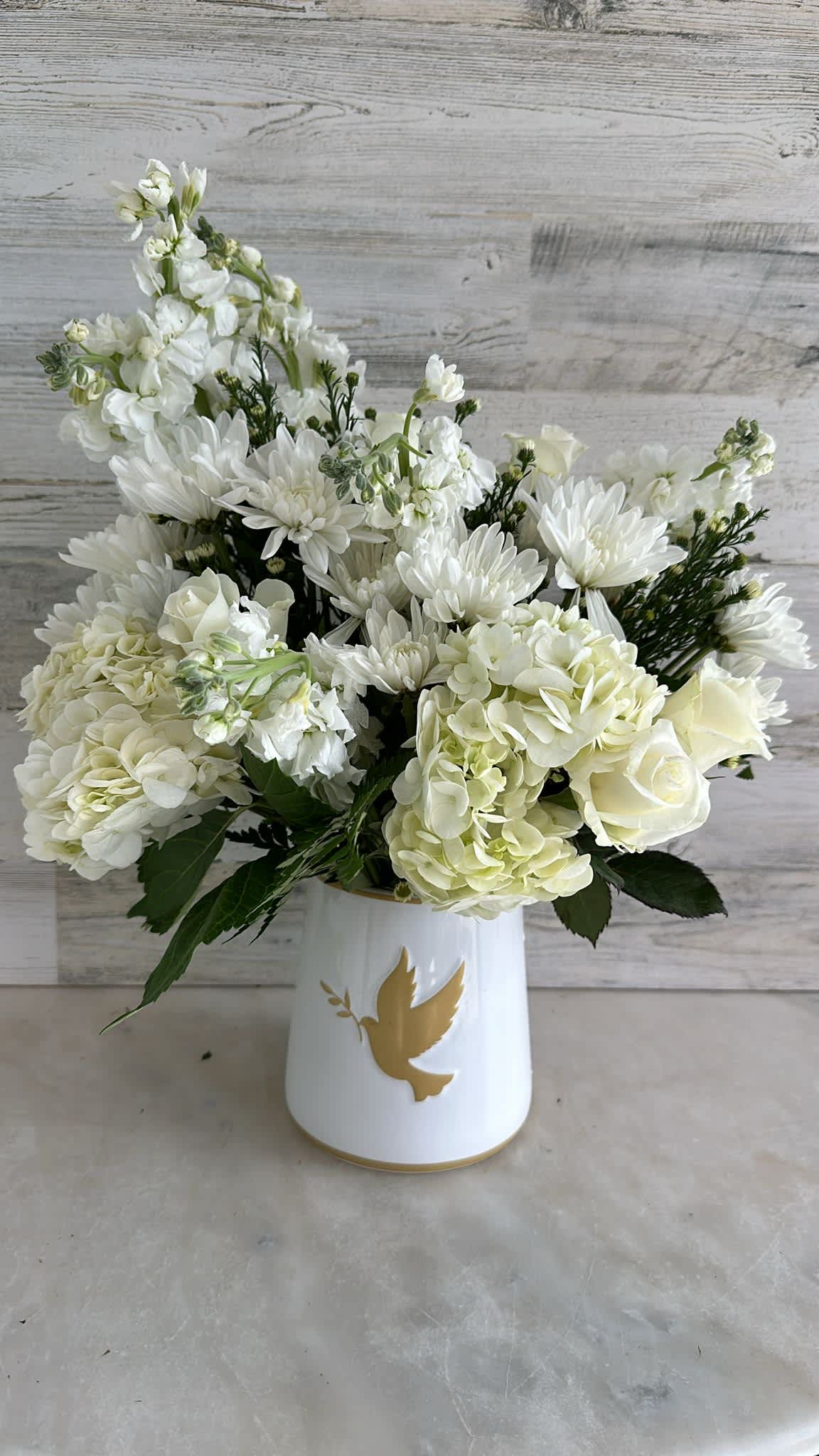 The Dove - white arrangement with a finest white ceramic container with a dove, the arrangement has hydrangeas, roses, stocks and mums