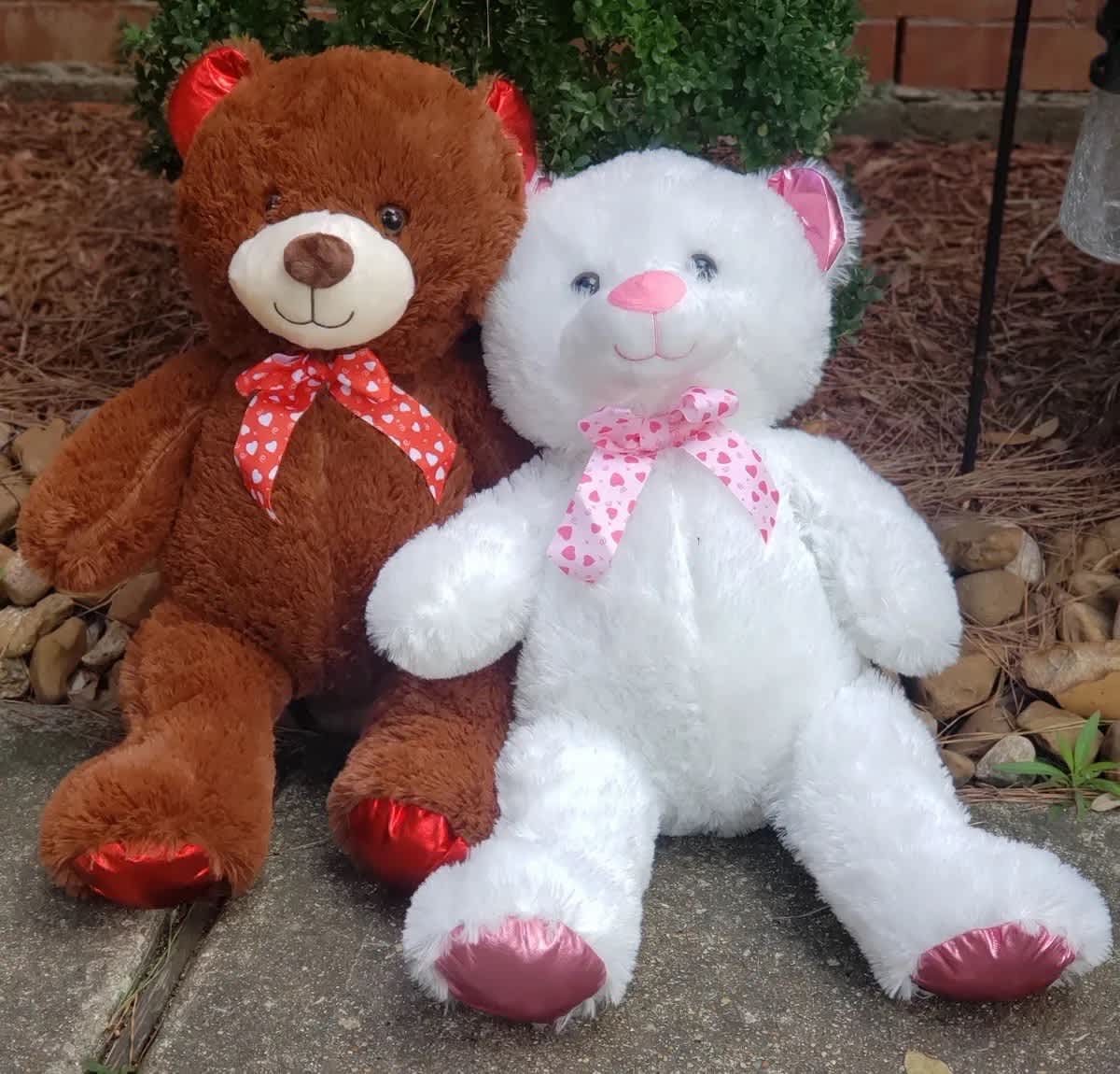 Two plush teddy bears sitting side by side, one brown and one white with heart-patterned bows.