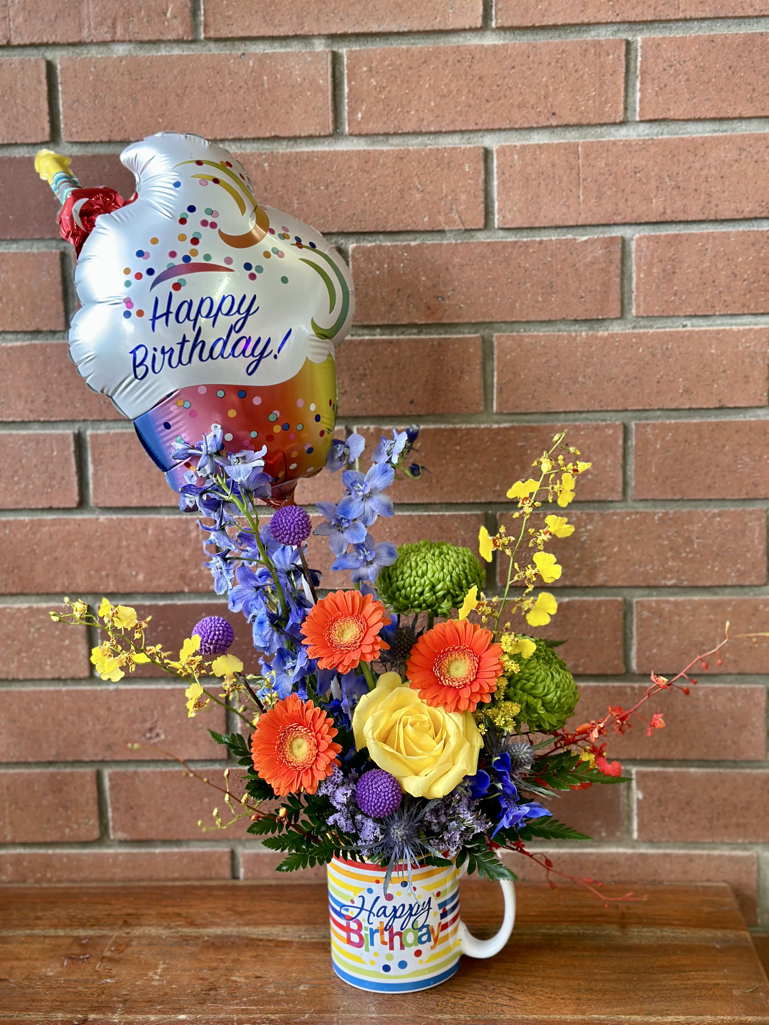 Happy Birthday Mug & Balloon Happy Birthday Mug & Balloon - Wish your special loved one a very Happy Birthday with our beautiful birthday mug bouquet - colorful blue delphinium, yellow orchids, yellow roses, orange gerbers, green ball mums and lush greenery and filler flowers. Accented with a festive Birthday 9” Balloon.