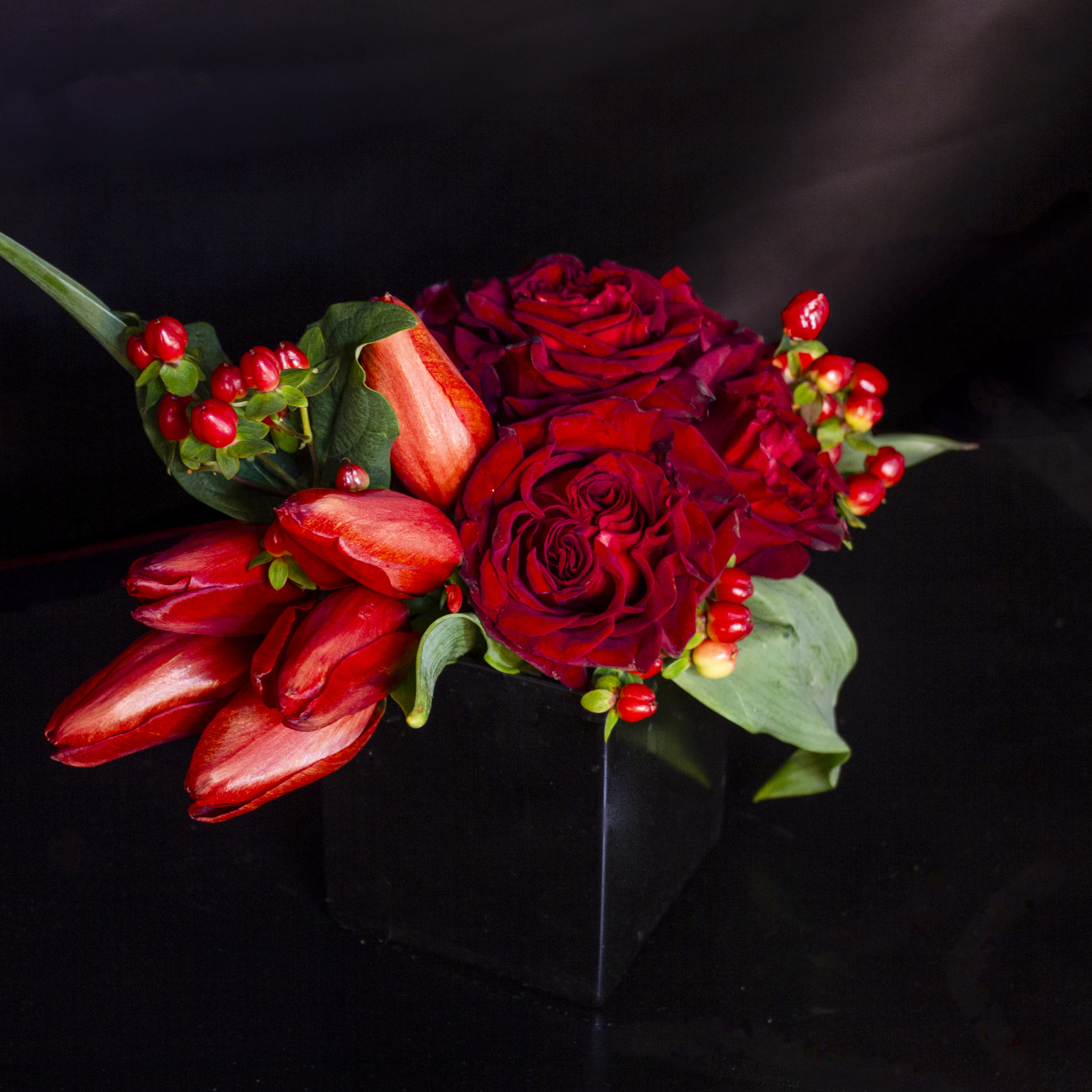 'Be My Valentine' by Madison's Flowers - Ask that special someone to “Be my Valentine” with sweet red tulips, passionate crimson Heart roses, and pops or bright red hypericum berries. The perfect sentiment for that sentimental individual in your life. A Madison’s Flowers original for 2024. Vase is approx. 4x4x4.