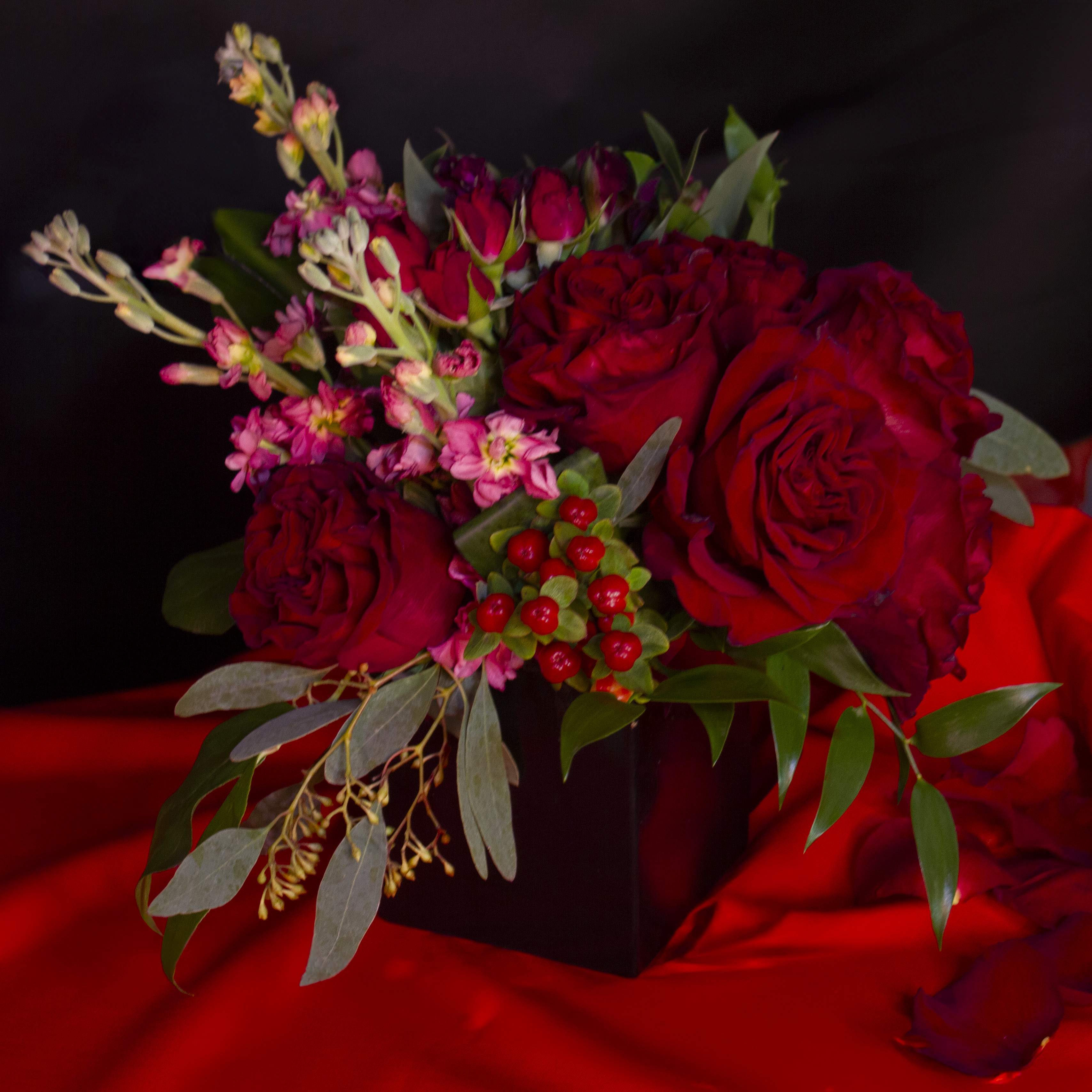 'Grand Rouge' by Madison's Flowers - Fluffy red Heart roses, sweetheart scarlet spray roses, bright red hypericum berries, and beautiful moody mauve stock come together in a petite but stately black glass cube. This compact style has all the impact of a Parisian crimson cabaret. Send sexy today. A Madison’s Flowers original. Vase is approx. 4x4x4.