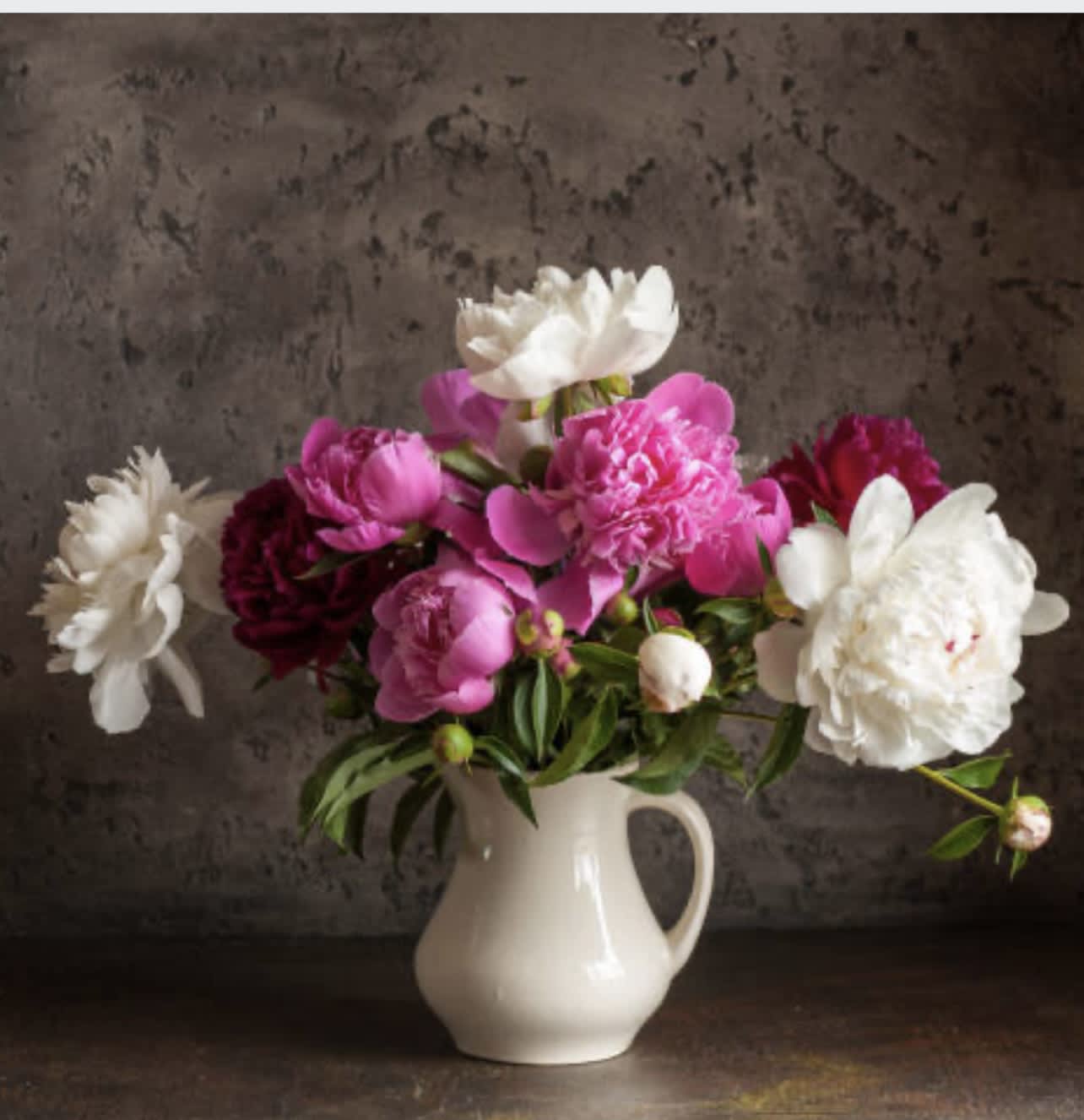 Pitcher of Peonies - White pitcher with red and white peonies, hot pink and light pink ranunculus. Greens may be needed to create fullness in vessel.