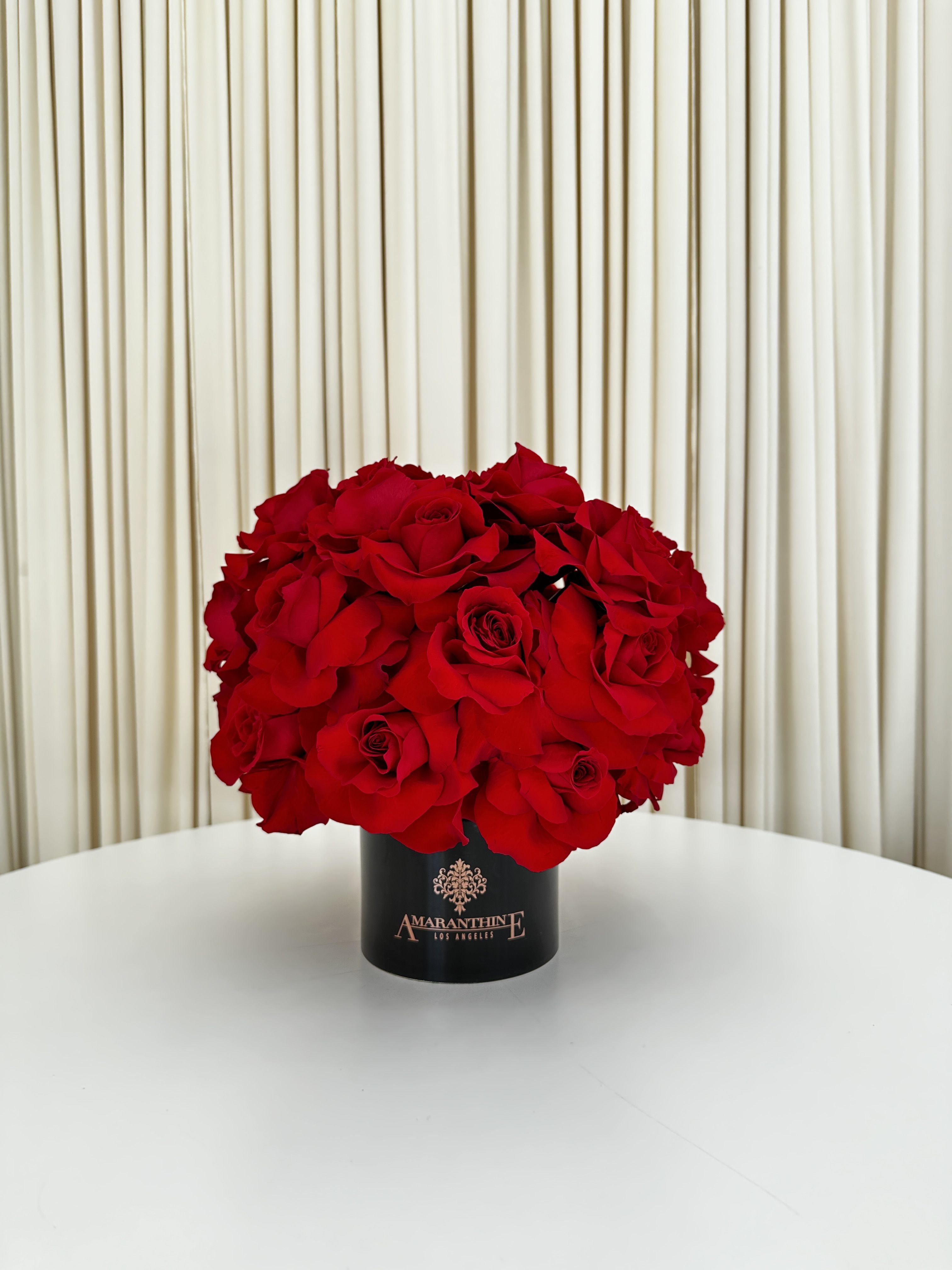 Scarlet Elegance - This exquisite arrangement of red roses is the epitome of elegance and beauty. The vibrant red petals of the roses create a striking contrast against the black ceramic vase, making it a captivating centerpiece for any room. The carefully arranged roses exude a sense of romance and passion, making it an ideal gift for a loved one or a charming addition to your own home decor. (arrangement is 360 degrees )