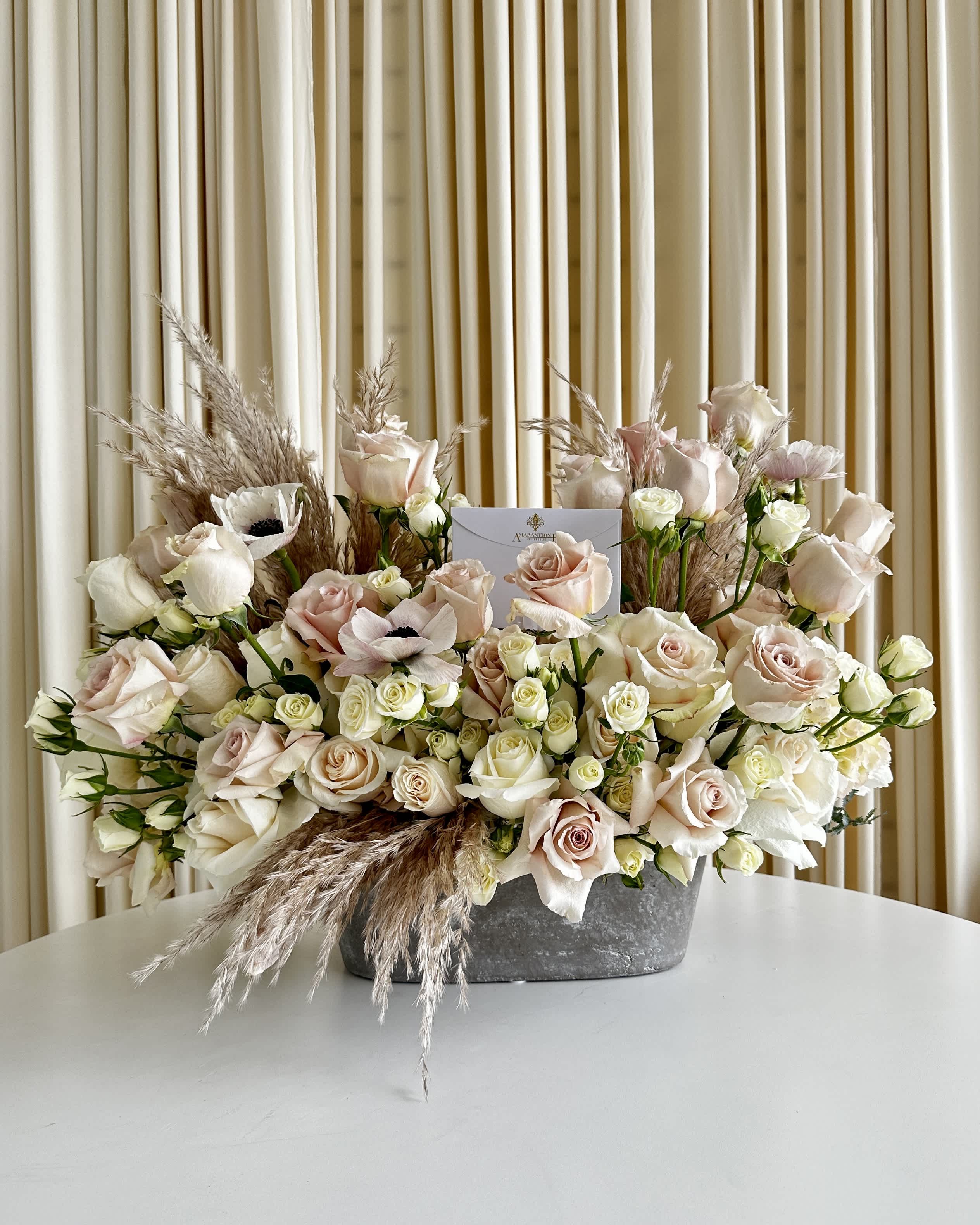 Rustic Reverie - Immerse yourself in the allure of &quot;Rustic Reverie,&quot; our exquisite floral arrangement that marries the soft hues of neutral roses and anemones in a rustic metal vase. This captivating ensemble transcends trends, embodying a classic beauty that stands the test of time. The neutral palette speaks of understated sophistication, while the rustic metal vase adds a touch of charm and character. Bring the essence of timeless beauty into your space with this carefully curated arrangement that effortlessly blends grace and rustic reverie. Elevate your surroundings and celebrate the enduring allure of nature's finest blooms.