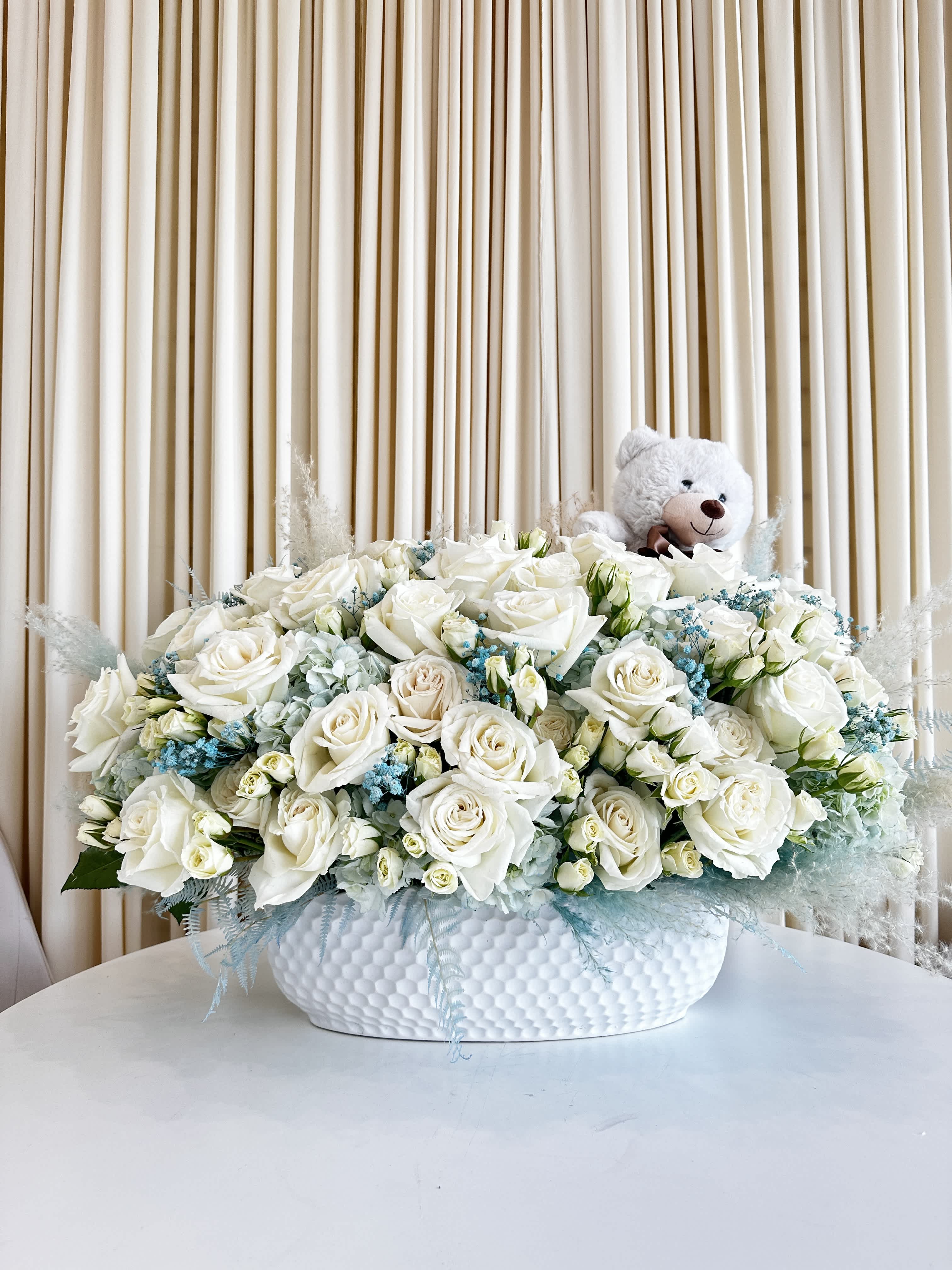 Bundle of Joy Blossom &amp; Teddy - Introducing our &quot;Bundle of Joy Blossom &amp; Teddy,&quot; the ultimate floral delight designed to celebrate the arrival of a precious newborn. Delicate, charming, and filled with love, this enchanting flower arrangement is the perfect way to extend warm congratulations to new parents.  Incorporating a serene palette of soft blues and pure whites, our expert florists have crafted a masterpiece that exudes serenity and innocence. Each bloom is carefully arranged to create an elegant display that captures the essence of this joyous occasion.  But there's more to this gift than just blossoms. Nestled amidst the fragrant flowers, you'll find an adorable keepsake teddy bear, the perfect companion for a little one. This cuddly teddy will serve as a lasting memento, bringing smiles to the family for years to come.  Our &quot;Bundle of Joy Blossom &amp; Teddy&quot; is not just a gift; it's a heartfelt gesture that welcomes a new life into the world. Whether you're gifting it to friends, family, or colleagues, this arrangement is sure to touch hearts and convey your warmest wishes.
