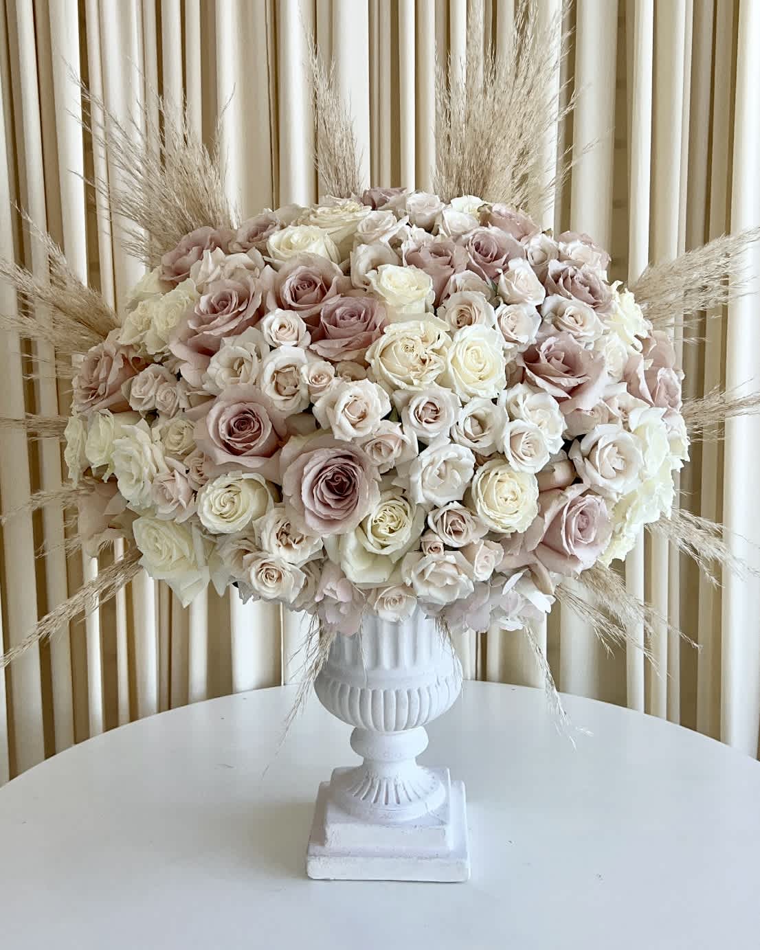 Serene Whispers Serene Whispers - Indulge in the gentle beauty of our "Serene Whispers" flower arrangement, thoughtfully designed to captivate your senses. Delicate neutral-colored roses and hydrangeas come together in perfect harmony within a stunning white pedestal vase, exuding an air of elegance and tranquility. To add a whimsical touch, we've incorporated a hint of pampas, gently swaying like whispers of serenity. Elevate your space with this exquisite masterpiece, a captivating blend of grace and charm that will leave you enchanted.