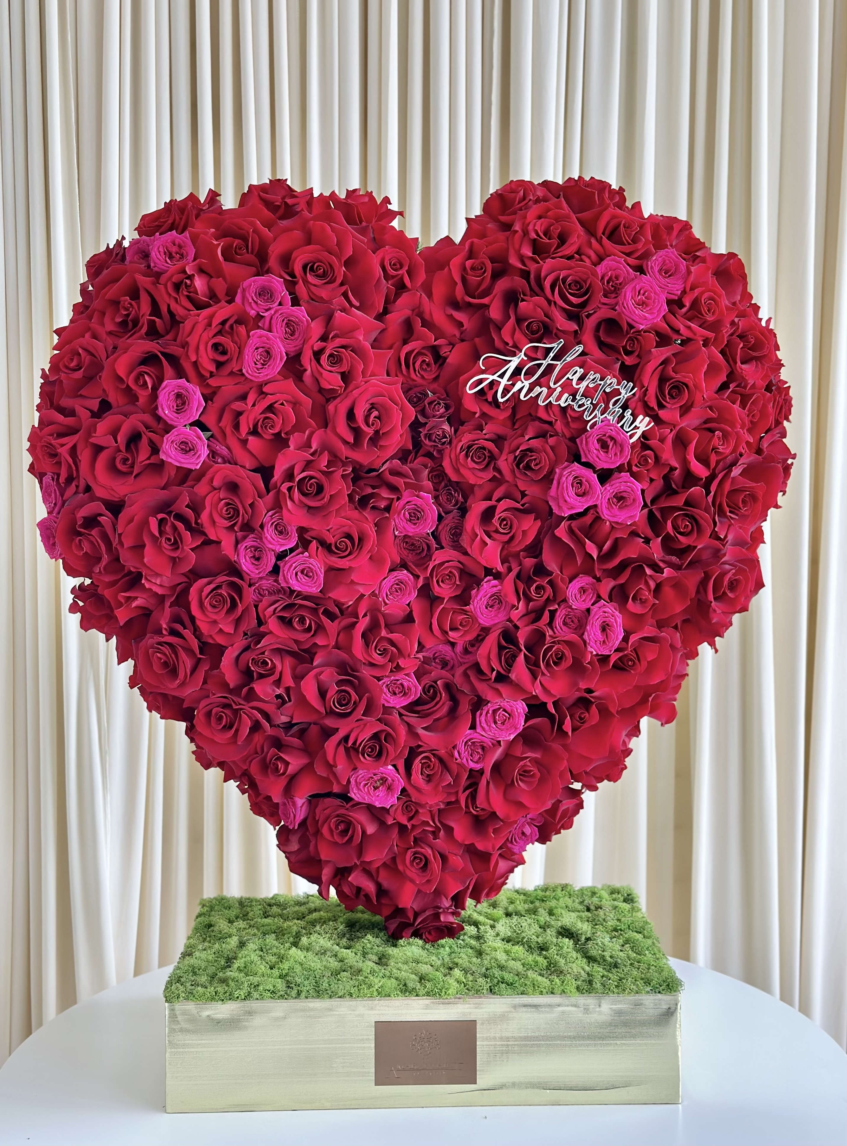 Romantic Radiance - !!! Happy Anniversary not included!!! Ignite the flames of love with our &quot;Romantic Radiance&quot; Heart-Shaped Anniversary Arrangement. Crafted with care, this captivating arrangement features a lavish display of red and fuchsia roses, delicately arranged to form a heart shape, symbolizing your boundless love and affection. Adorned with a gleaming &quot;Happy Anniversary&quot; in gold, this arrangement becomes an expression of your everlasting commitment and joyous journey together. Celebrate your special day with the romantic allure of &quot;Romantic Radiance&quot; and cherish the memories forever. 