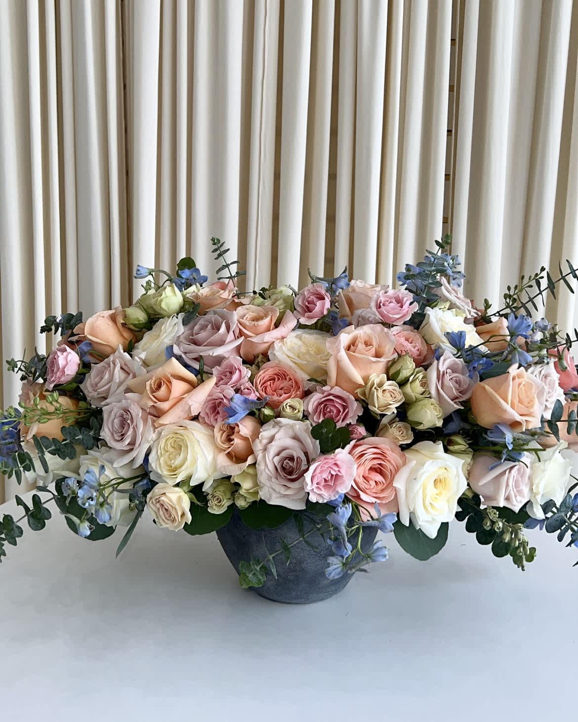Sunshine on a Cloudy Day - A lovely summer arragement to brighten up anyones day. A bright set of peaches, blues, whites, and nudes designed in a beautiful charcoal pot.  