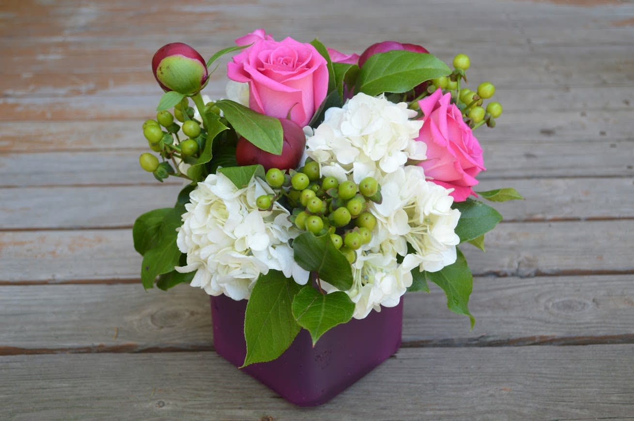 Hot Pink peonies, pink roses and hydrangea in a Square Vase - Hot pink peonies, pink roses, white hydrangea, and green hypericum berries arranged in a 4&quot; square glass cube. This is a low tight arrangement perfect for that small space such as a  small table, desk, or side table. 