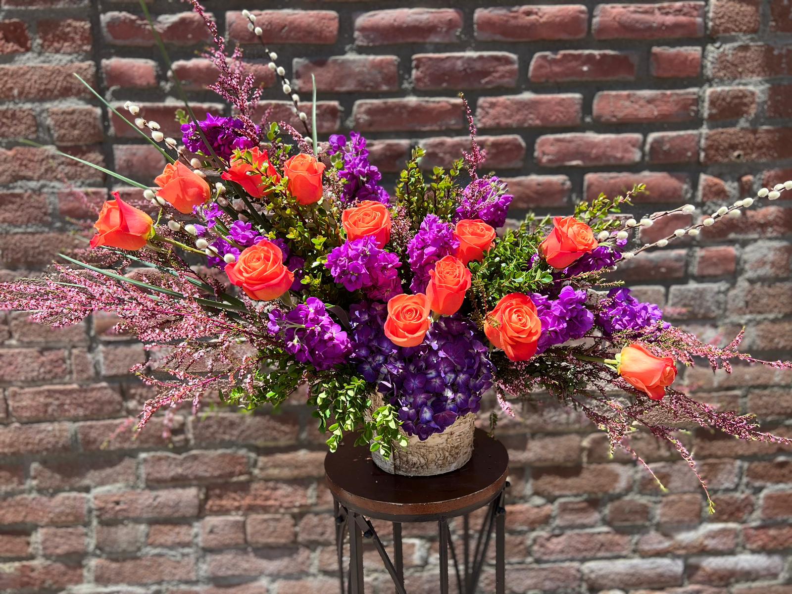Orange Crush  - composed of 12 orange roses, dark purple stock, calcinia and stock , boxwood , pussy willow and purple hydrangea all in a birch container