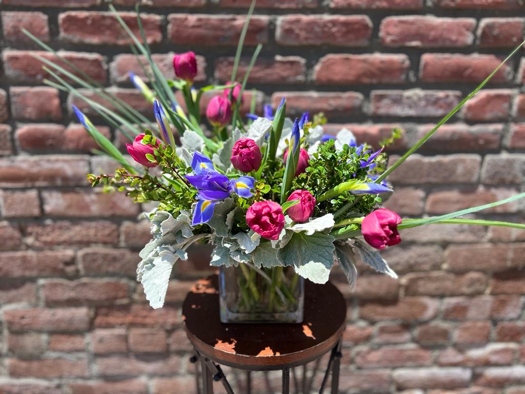 Old World Garden Old World Garden - Composed of one dozen purple or blue iris, Dark pink tulips, dusty miller and boxwood all presented in a glass cube vase