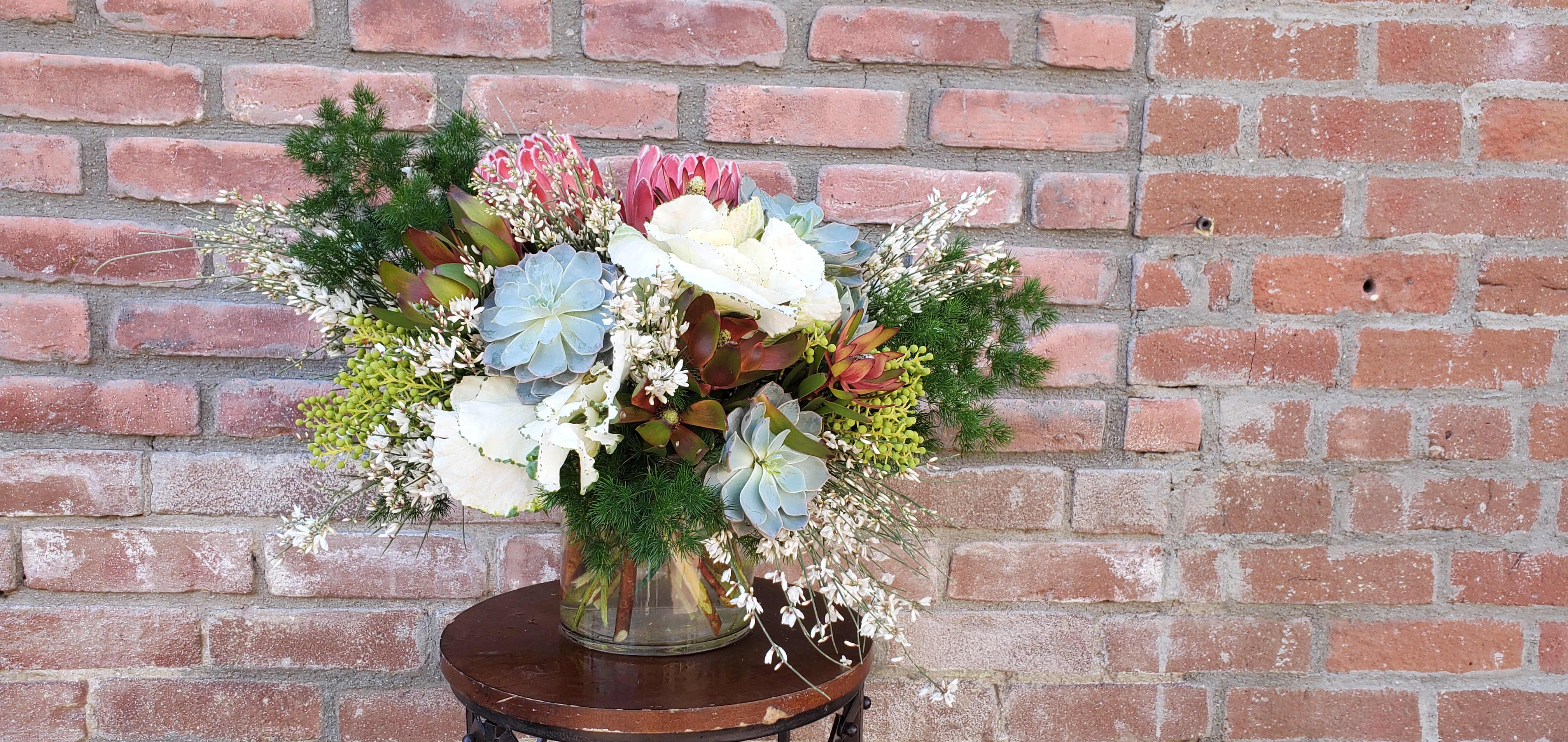 feels like fall feels like fall - composed of ming fern, pink proteas, kale, safari sunset, french broom , barazillian berries and succulents in a cylinder vase