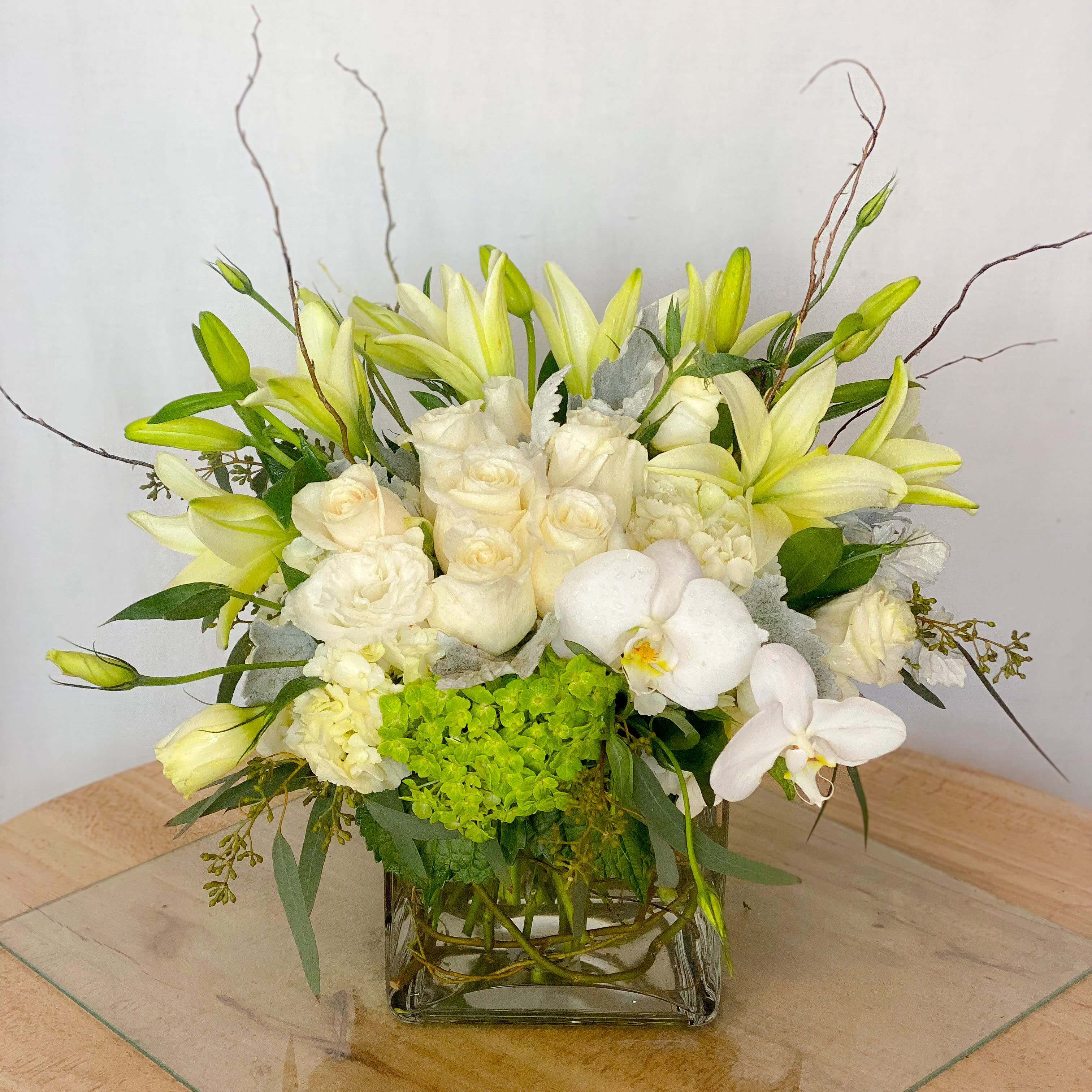 White Exotic - An all white bouquet designed with lush hydrangeas and roses with phalaeonopsis orchids and curly willows arranged in a keepsake glass cube vase. Beautiful, exotic and absolutely stunning! Surprise your loved one today by ordering for same day delivery! Guaranteed to impress!  Approximately 14” D