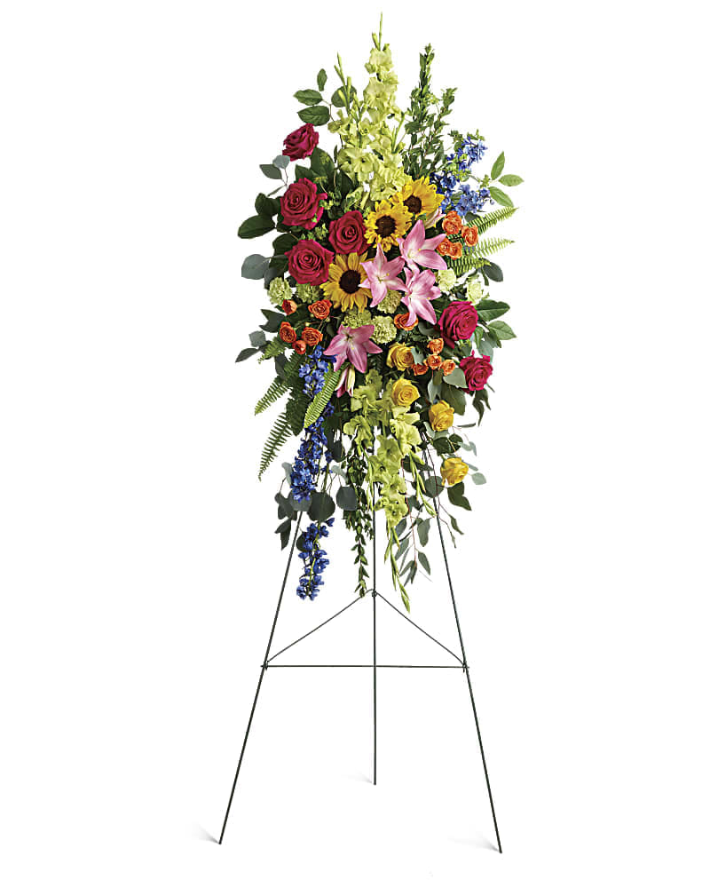Radiant Colors Spray - Bursting with joy this radiant spray of rainbow blooms is an exuberant tribute to never-ending love. This spray features hot pink roses yellow roses orange spray roses pink asiatic lilies green gladioli green carnations medium yellow sunflowers blue delphinium bupleurum myrtle sword fern silver dollar eucalyptus and lemon leaf. Delivered on a wire easel.