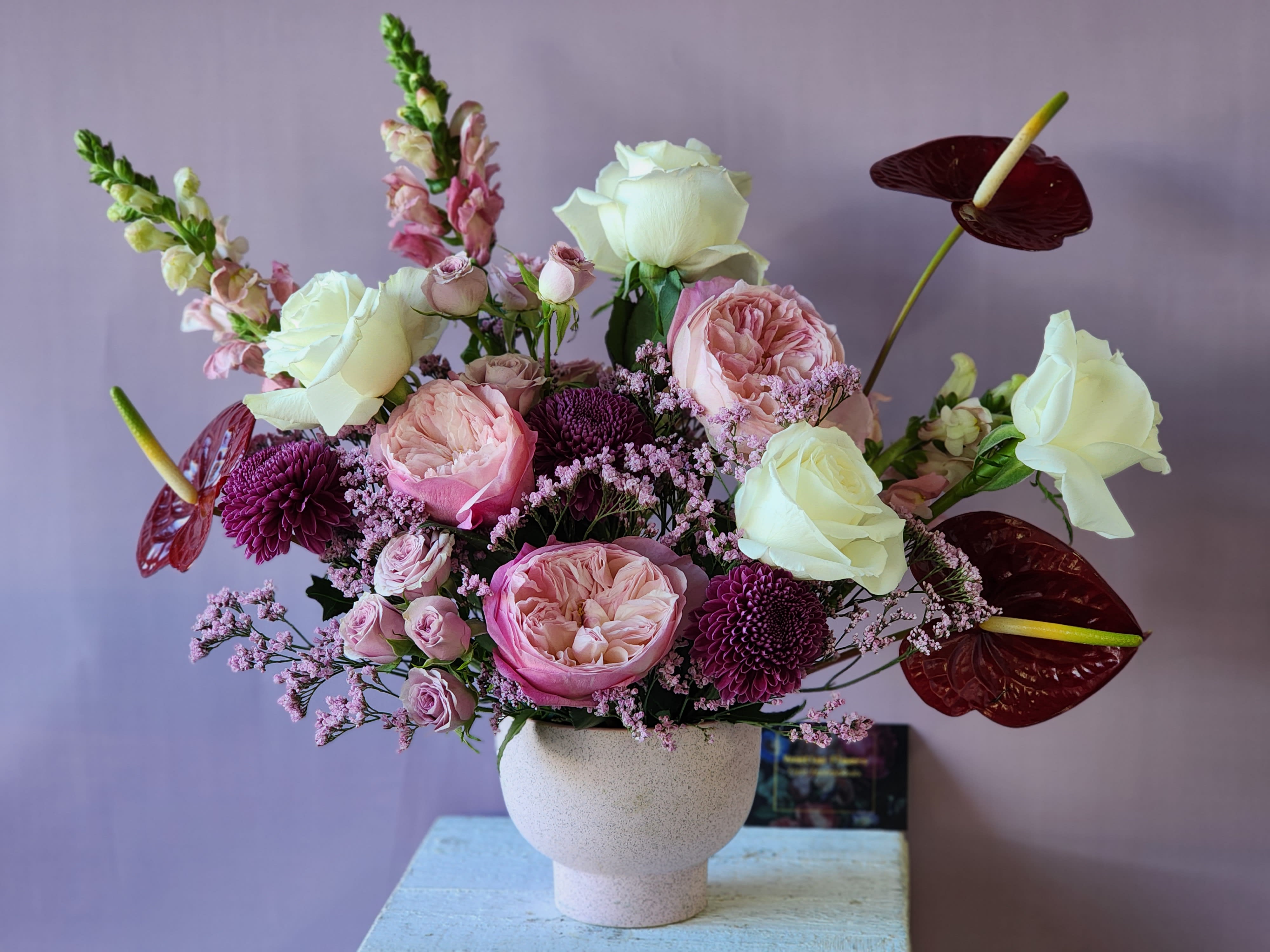 Lush Love  - Romantic arrangement in a modern pink vase with gorgeous pink Garden roses, red anthurium, snap dragons, spray roses, cream roses, fillers and greenery 
