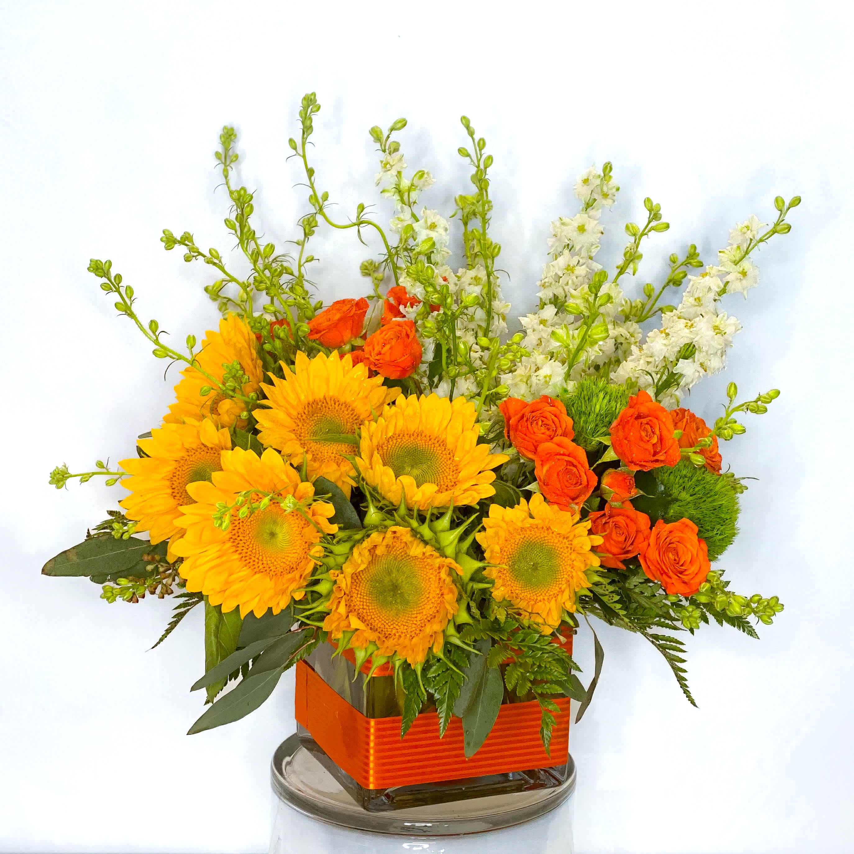 Perfect Sun  - Bright and lovely sunflowers arranged in a centerpiece style with orange equadorian roses, yellow snapdragon stems, green hypericum berries and lush greens. Gorgeously situated in a clear glass cubed vase accented with an orange woven edge grosgrain ribbon. This bouquet will be a warm wish of happiness for your special someone.   Approximately 14&quot; H x 10&quot; W
