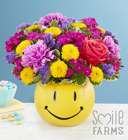 You Make Me Smile Bouquet -  Helping you deliver smiles is what we do…and this feel-good bouquet is a great way to do it! Bunches of blooms in uplifting colors are gathered into our keepsake smiley face container, delivering just the brightness they need to make their day better. Perfect for celebration-worthy moments.