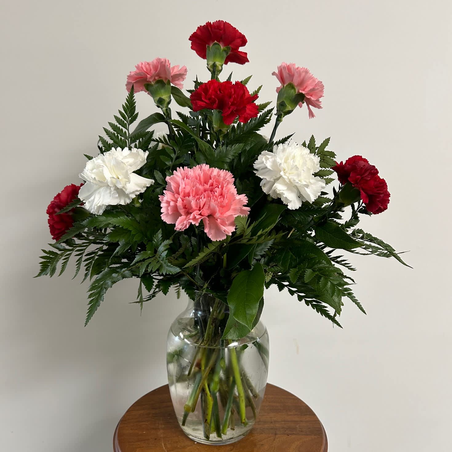 12 Carnations Assorted colors - Sweetly fragrant, this simple arrangement is sure to charm!   A dozen ASSORTED carnations arrive professionally arranged in a clear sweetheart glass vase.  A MIX OF VALENTINE COLORS WILL BE USED FOR VALENTINE'S DAY.
