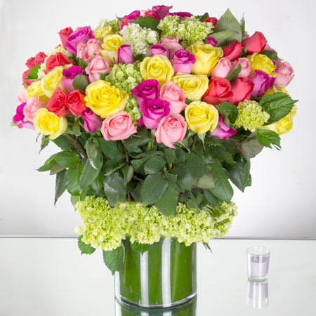 Lush Abundance  - Prepare to be captivated by the sheer beauty and abundance of this extraordinary flower arrangement. Featuring 100 assorted roses in a splendid array of colors, complemented by delicate mini green hydrangea, all elegantly showcased in a large, transparent cylinder vase.   The Roses: *   **Assorted Roses**: This arrangement boasts an impressive collection of 100 roses in a variety of captivating colors. From romantic shades of red and soft pinks, to vibrant yellows, tranquil whites, and everything in between, this assortment of roses offers a rich visual tapestry that is sure to delight and enchant. Each rose is carefully selected for its freshness, beauty, and long-lasting quality, ensuring a truly remarkable display.   The Mini Green Hydrangea:     **Delicate Mini Green Hydrangea**: Nestled among the stunning roses is the charming addition of mini green hydrangea. These petite blooms add a touch of freshness and an unexpected pop of color that beautifully complements the vibrant roses. The mini green hydrangea symbolizes harmony and renewal, enhancing the overall visual impact of the arrangement.   The Vase:  The flowers are arranged in a large cylinder vase, allowing for a grand and eye-catching presentation. The transparency of the vase accentuates the natural beauty of the roses and hydrangea, adding a modern and sleek touch to the arrangement. The large size of the vase provides ample space for the abundant bouquet, ensuring a stunning focal point that will attract attention from every angle.  This flower arrangement of 100 assorted roses, mini green hydrangea, and a large cylinder vase is an opulent display of beauty and elegance. Perfect for grand celebrations, weddings, or a statement piece for a special event, the sheer abundance of roses and the delicate allure of the mini green hydrangea creates an unforgettable visual experience. Let the extravagance of this arrangement take center stage and leave a lasting impression on all who behold it.   