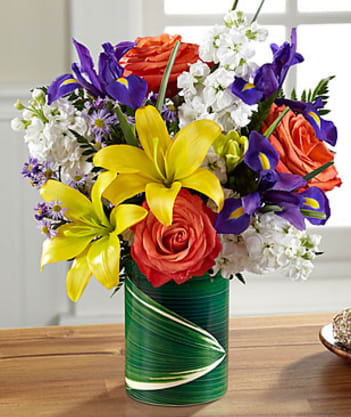 Spark - Bright, crisp and high contrast flowers are combined in a lively, happy-making bouquet that's a treat to give or get for any reason at all. Yellow Asiatic lilies, purple iris, white stock, lavender Monte Casino, orange mini carnations (in Good only) and roses (in Better, Best and Exquisite) are arranged in a ceramic &quot;illusion&quot; vase that convincingly replicates the look of a leaf-lined glass pillar. It's an arrangement sure to cast a golden glow to make any day one that's special and memorable.  LF4D