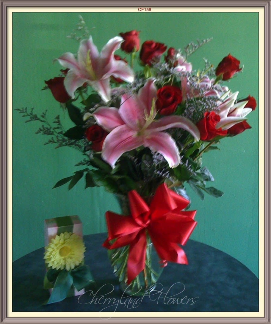 CF159 - Enchant your sweetheart with this lovely assortment of red roses, pink stargazer lilies, and foliage artfully arranged in an elegant glass vase adorned with a red bow. 